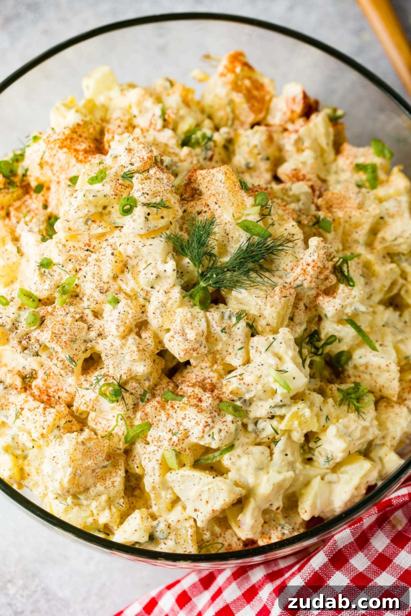 Secrets to the Best Potato Salad Ever 5 A glass serving bowl filled with potato salad. There are chunks of potato, chopped pickles, chopped eggs and dill in the salad. Paprika and fresh parsley is sprinkled on top.