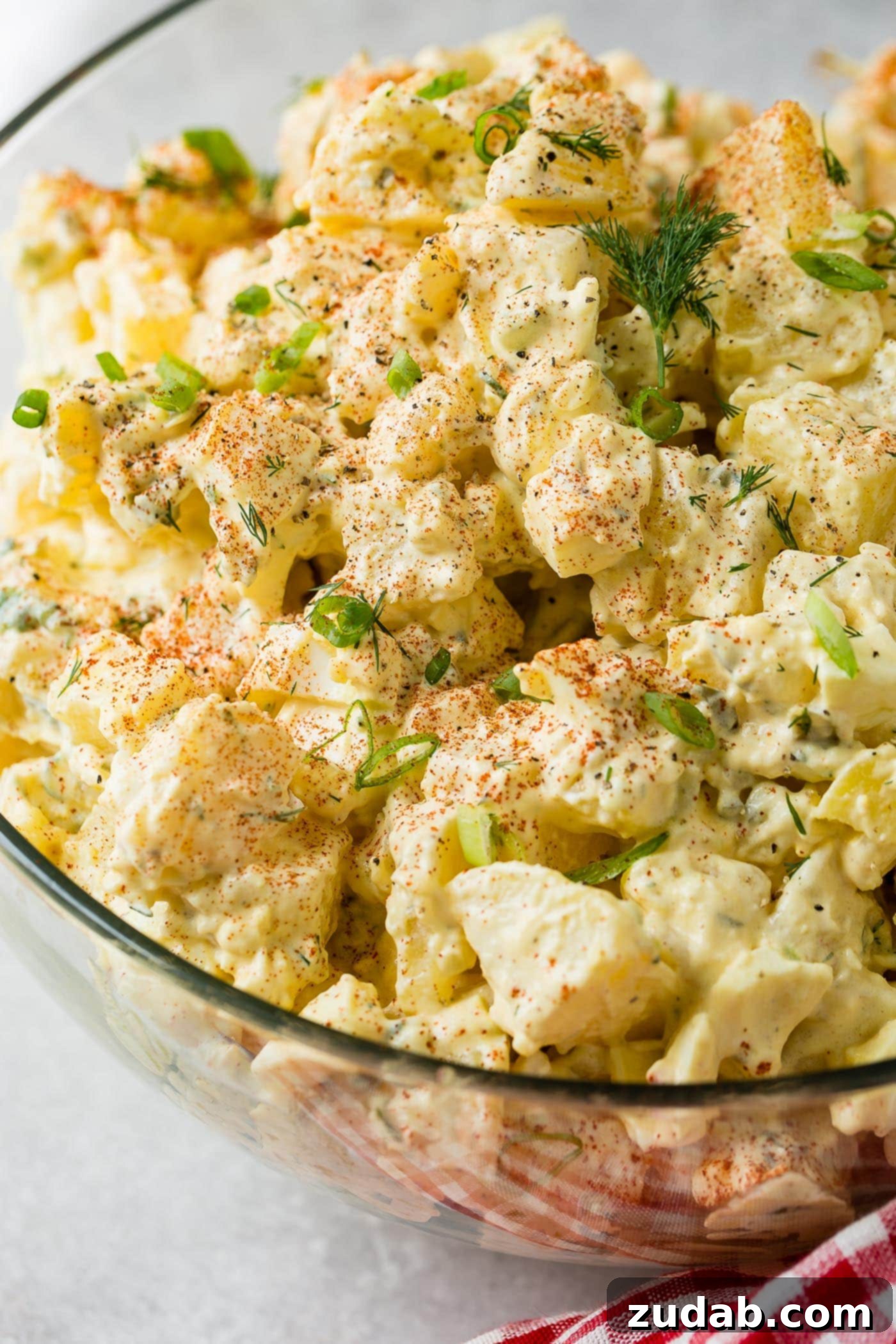 Secrets to the Best Potato Salad Ever 6 A glass serving bowl of potato salad. The chunks of potato, pickles, and eggs are topped with sprinkled paprika and fresh parsley.