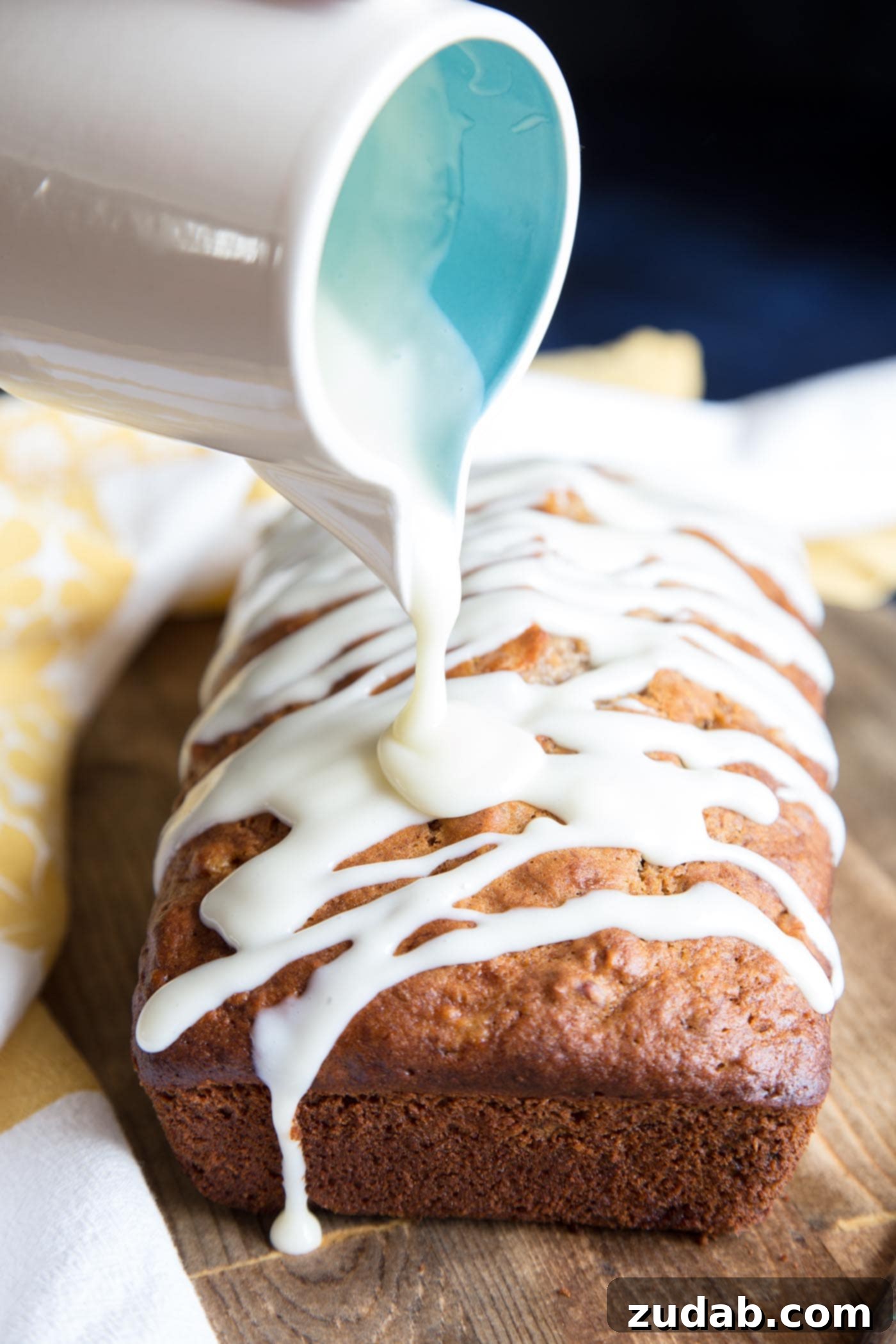 Hummingbird Banana Bread 4 Cream cheese glaze being artfully drizzled over a fresh loaf of Hummingbird Cake Banana Bread, enhancing its appeal.