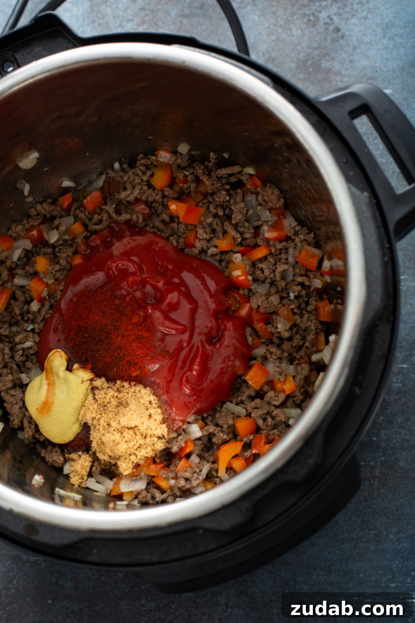 Sloppy Joe Mixture in Instant Pot An Instant Pot filled with browned hamburger, chunks of red bell pepper, and a rich sauce made from ketchup, Dijon mustard, and brown sugar, ready to be pressure cooked.