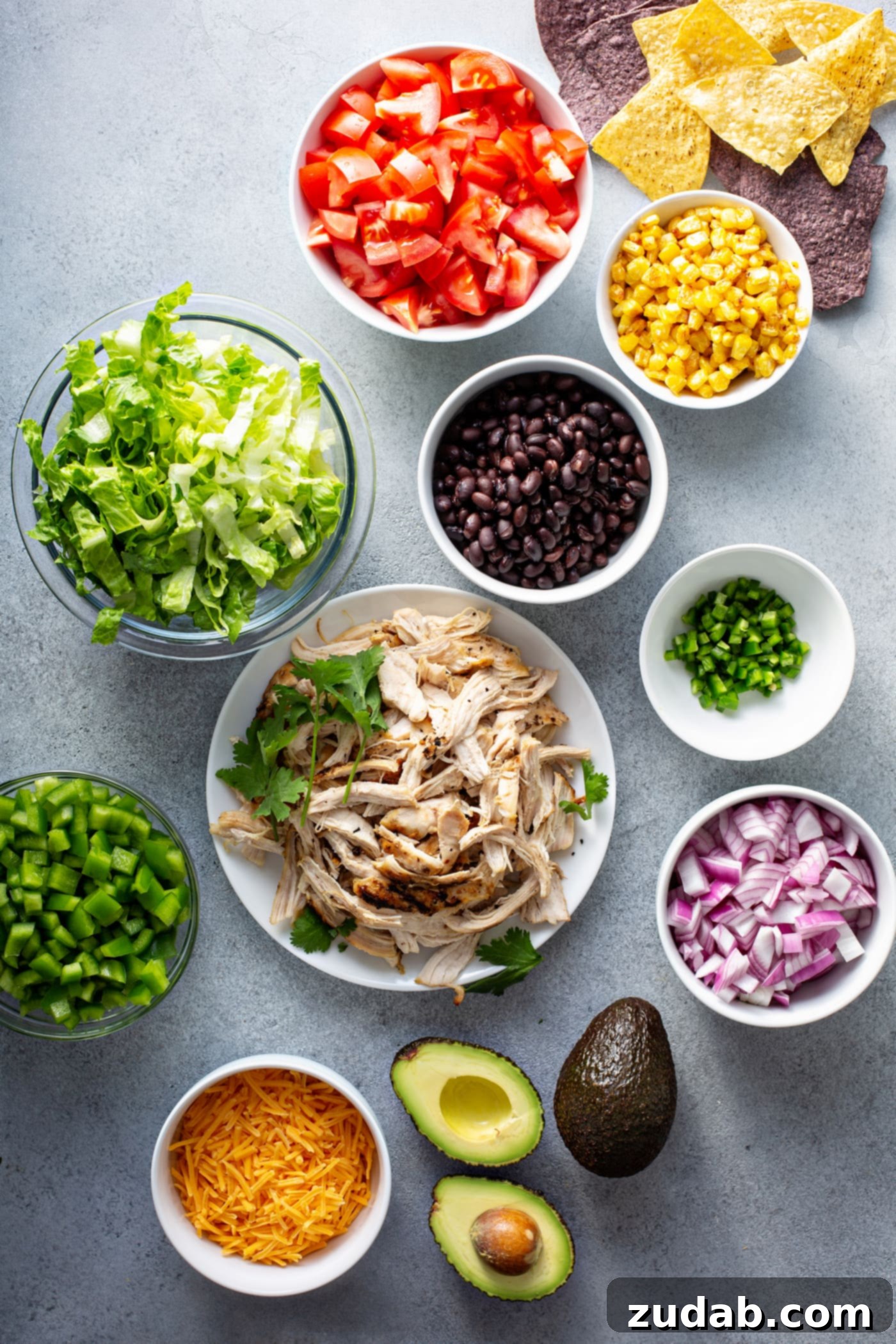 Simple Chicken Taco Salad Containers holding the ingredients for chicken taco salad. They contain corn, red onions, chicken, beans, bell peppers, taco seasoning, cilantro and there is an avocado on the table.