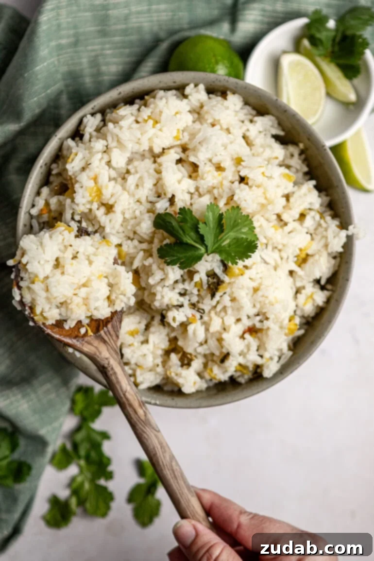 Restaurant-Quality Cilantro Lime Rice Just Like Café Rio 13 A photo of a large glass serving bowl full of fluffy cilantro lime rice, with a wooden spoon scooping out a generous portion. The rice appears perfectly cooked and garnished with fresh green cilantro, ready to be enjoyed.