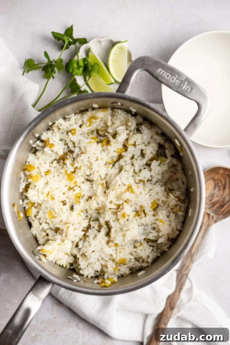 Restaurant-Quality Cilantro Lime Rice Just Like Café Rio 14 A large saucepan filled with freshly cooked, fluffy cilantro lime rice is shown, with a wooden spoon resting beside it. The rice is steaming gently, indicating its warmth and readiness to be served.
