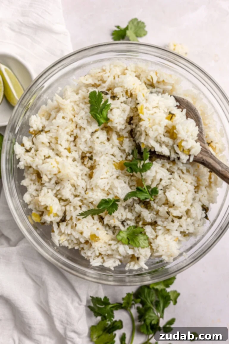 Restaurant-Quality Cilantro Lime Rice Just Like Café Rio 15 A close-up photo of a large glass serving bowl brimming with fluffy cilantro lime rice. A wooden spoon is seen scooping out a portion, highlighting the light and airy texture of the rice, ready for serving.
