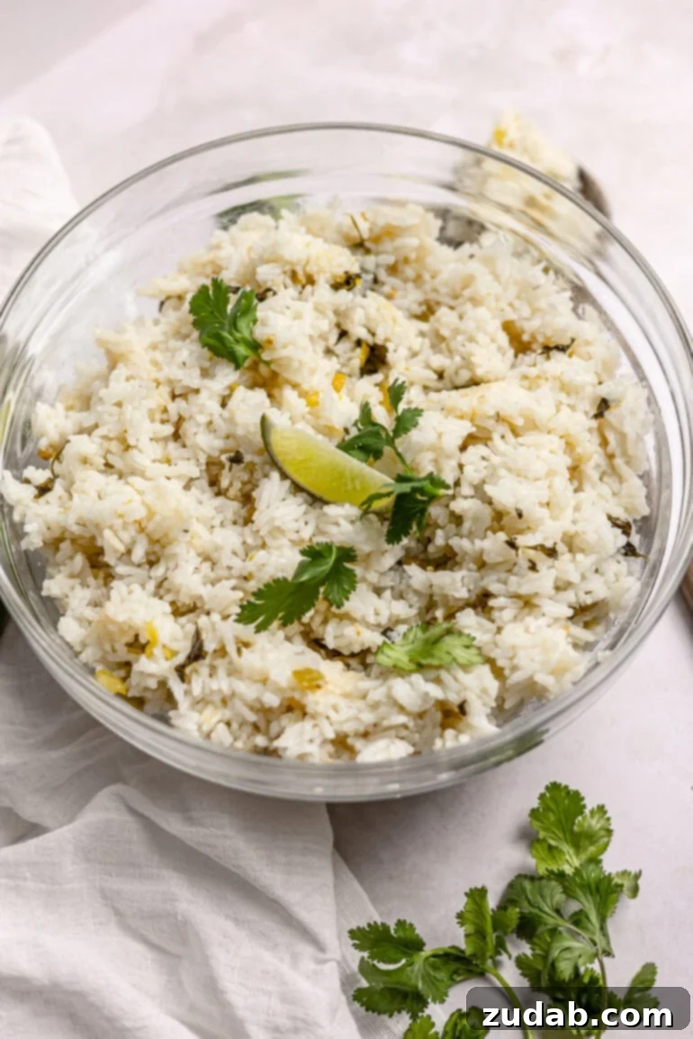Restaurant-Quality Cilantro Lime Rice Just Like Café Rio 3 A close-up photo of a large glass serving bowl filled with fluffy, bright green cilantro lime rice, elegantly topped with a generous sprinkle of fresh chopped cilantro and a wedge of vibrant lime. The textures and colors are visually appealing, highlighting the freshness of the ingredients.