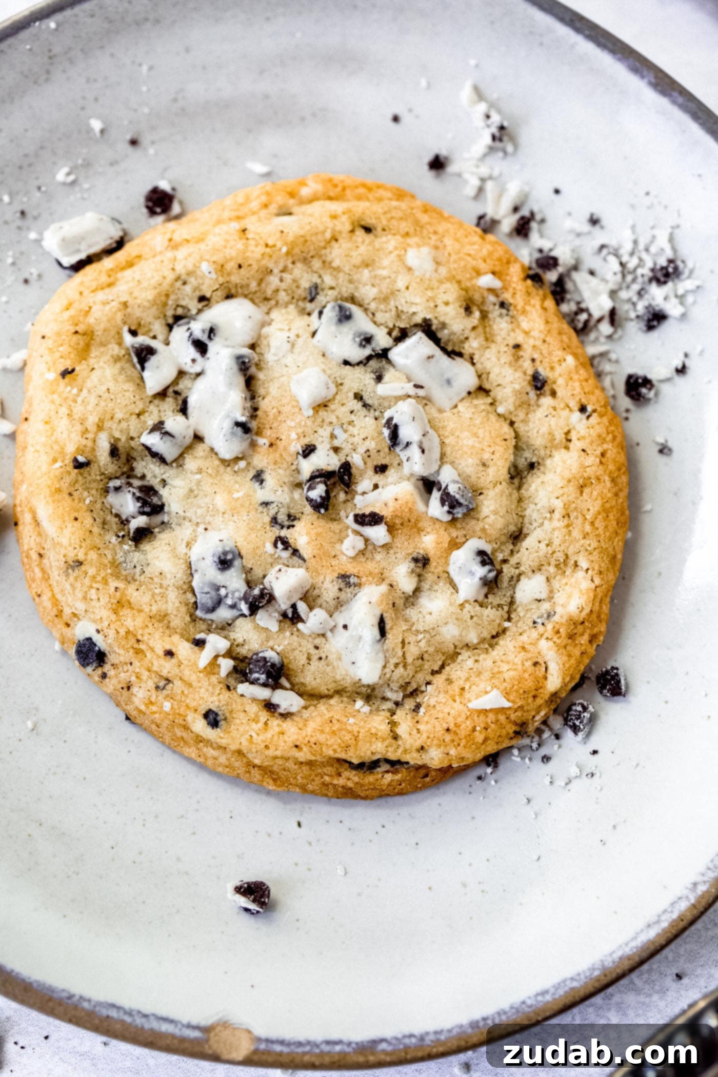 Loaded Cookies and Cream Cookie A large cookies and cream cookie, perfectly golden brown and loaded with visible chunks of cookies and cream candy bar, resting on a rustic wooden surface.