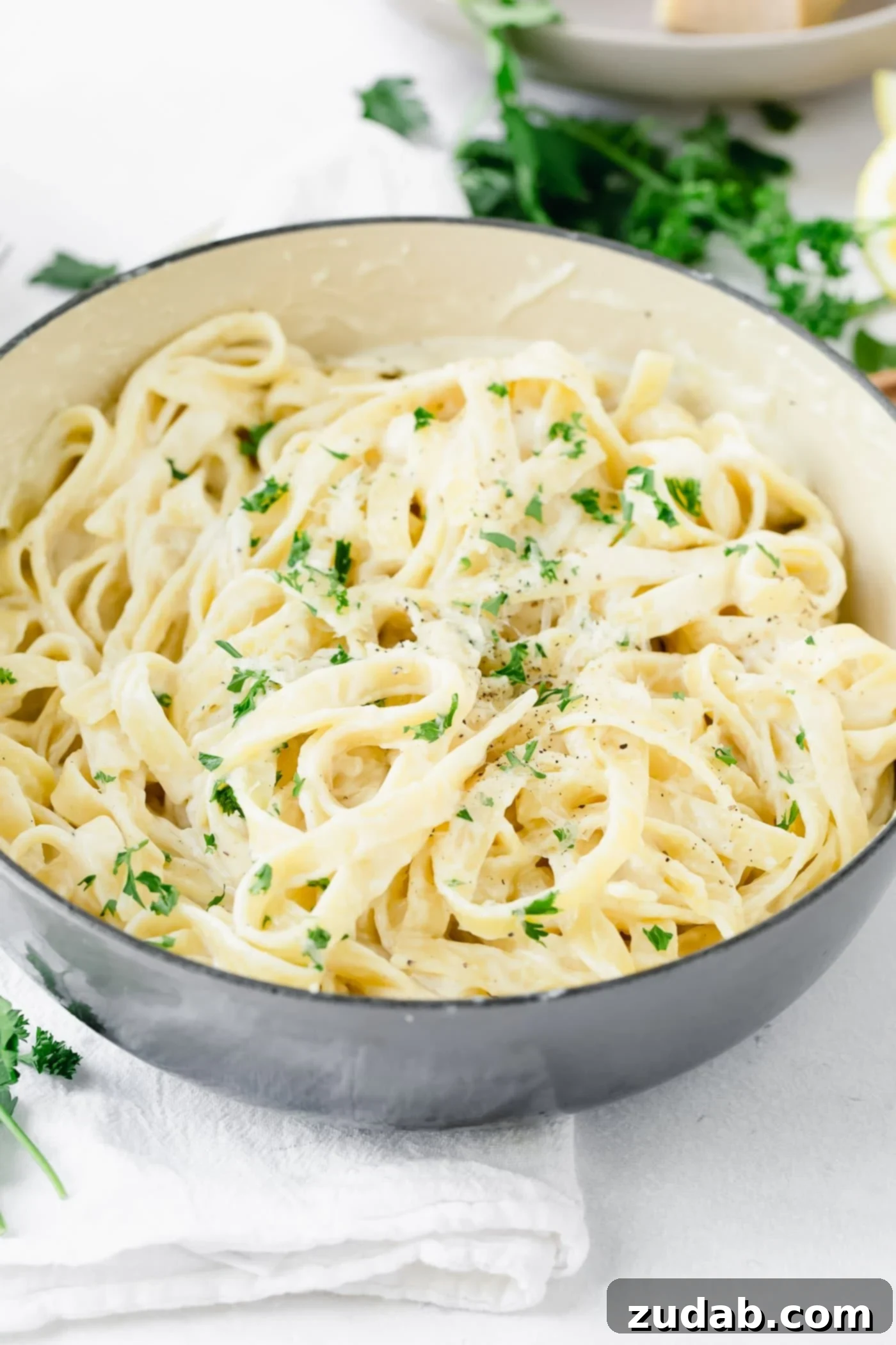 The Ultimate Velvety Alfredo Sauce 5 A bowl of fettuccine alfredo with a generous sprinkling of fresh parsley and a side of parsley leaves on a wooden table.