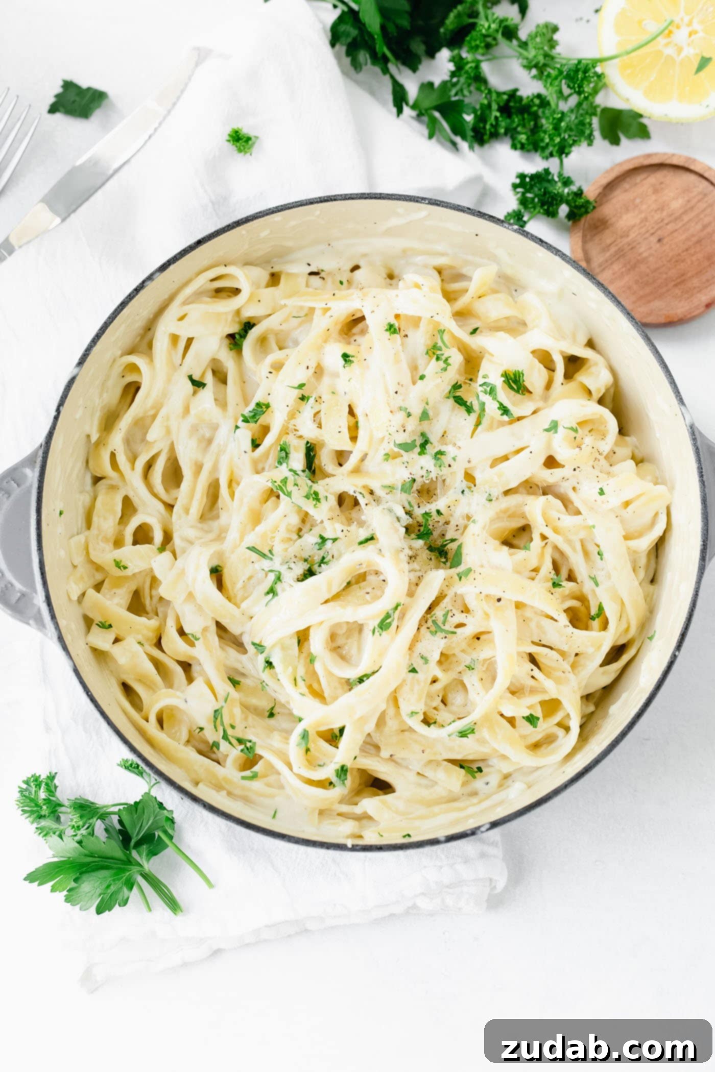 The Ultimate Velvety Alfredo Sauce 7 A bowl of fettuccine alfredo, garnished with fresh parsley, with lemon wedges and more fresh parsley on the side.