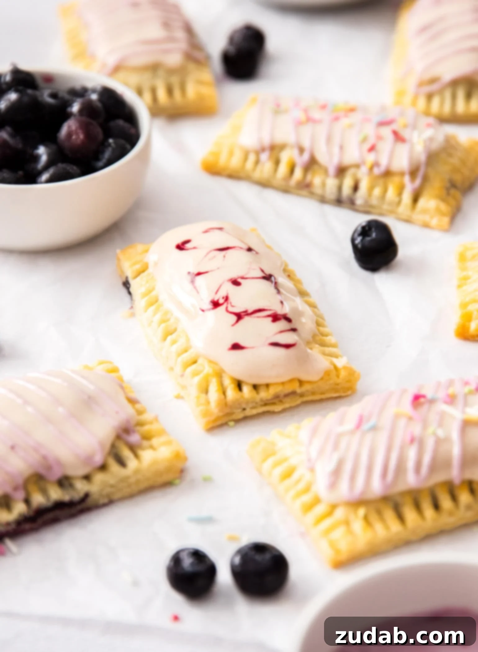 DIY Blueberry Toaster Pastries 2 A batch of homemade pop tarts on a sheet of white baking paper. A small white bowl of blueberries.