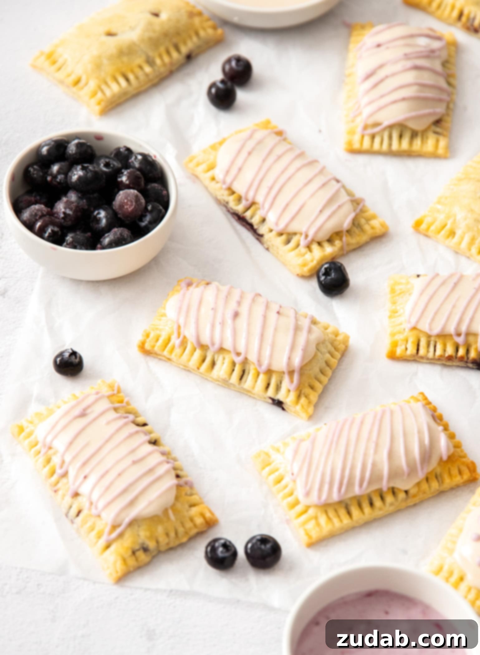DIY Blueberry Toaster Pastries 7 A batch of homemade pop tarts on a sheet of white baking paper. A small white bowl of blueberries.