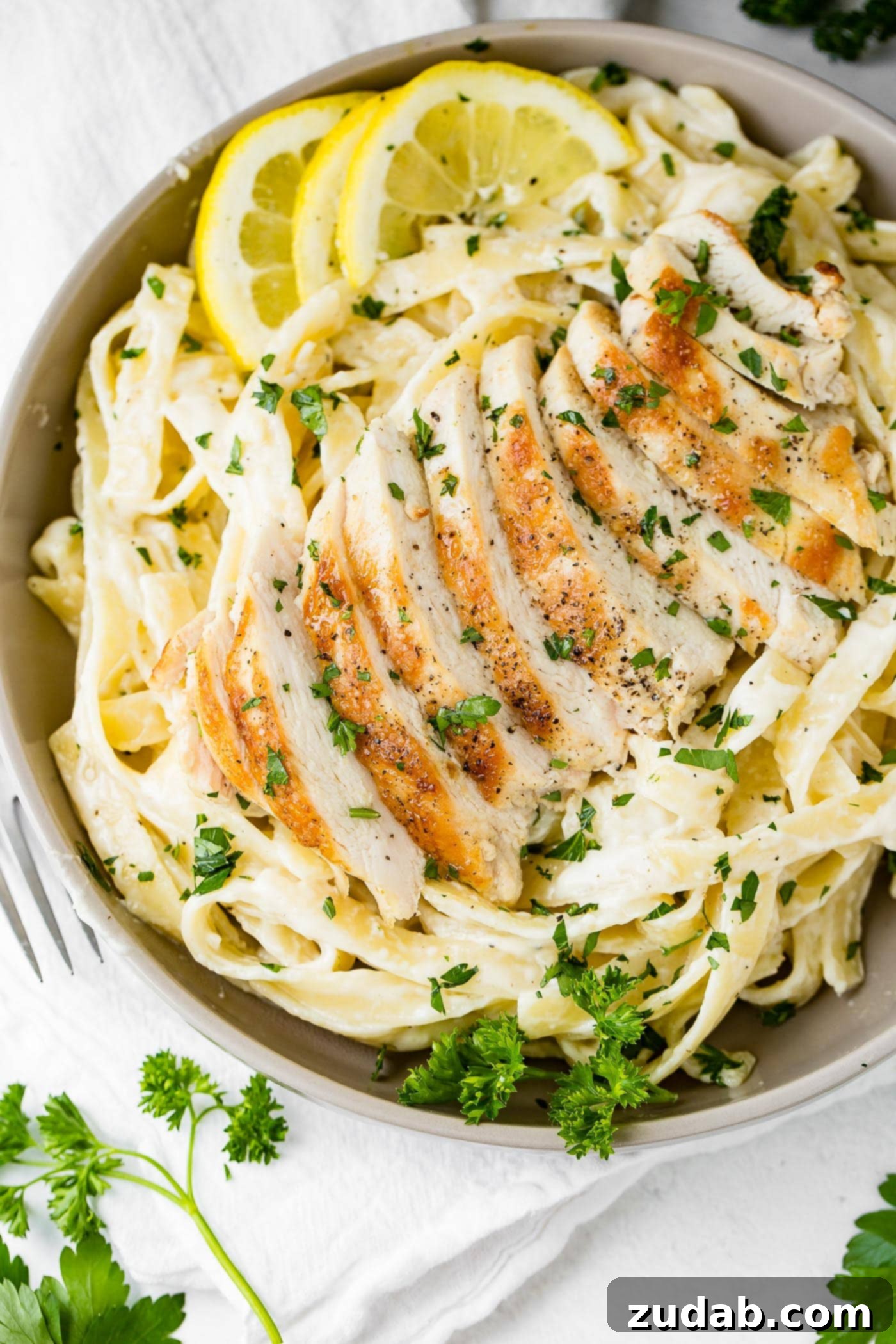Chicken Fettuccine Alfredo A close-up of f=chicken fettuccine alfredo. The pasta has slices of chicken resting on top and the whole dish is sprinkled with fresh parsley leaves.
