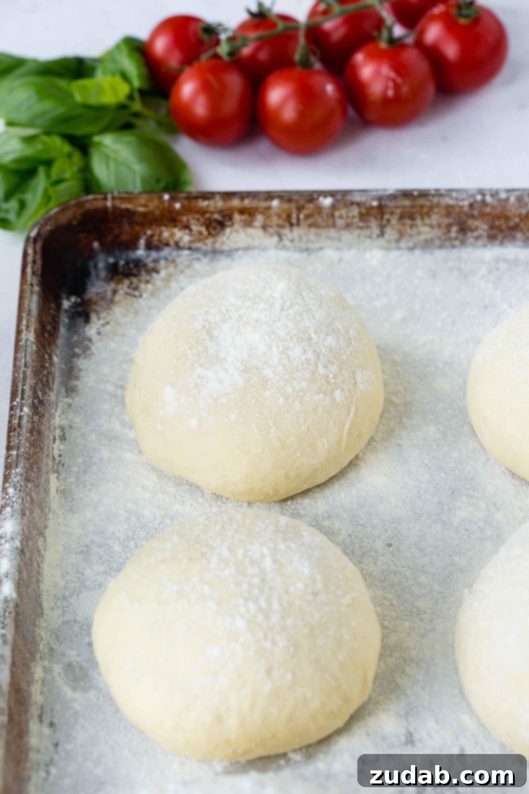 Four perfectly portioned balls of pizza dough rest on a lightly floured baking sheet, ready for their journey to become delicious pizzas.