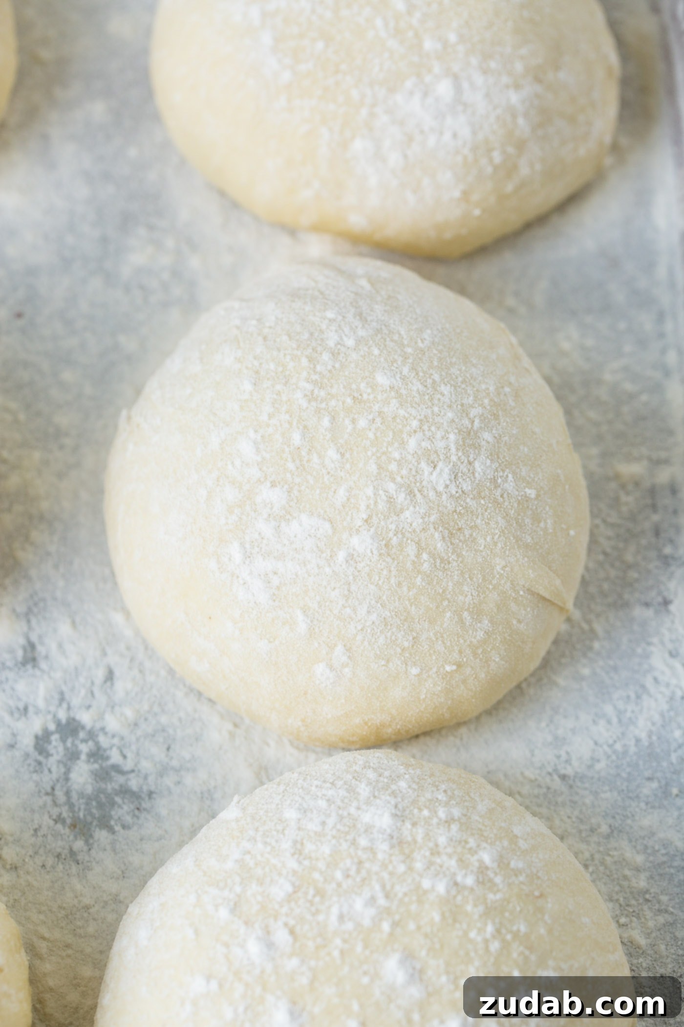 Three perfectly formed balls of pizza dough rest on a lightly floured cookie sheet, patiently waiting to be transformed into delicious pizzas.