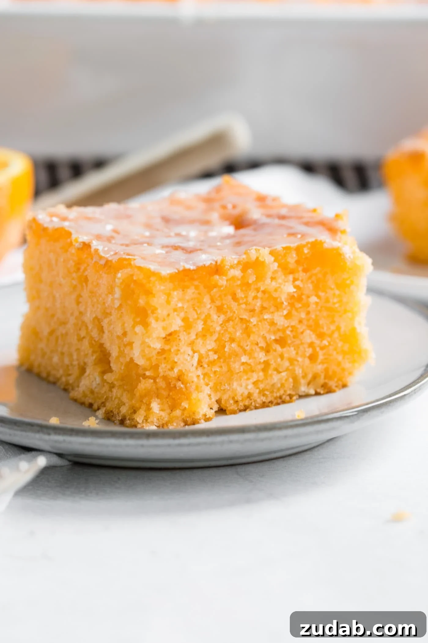 Delicious Orange Jello Cake A vibrant slice of Orange Jello Cake on a small white plate, adorned with a glossy orange glaze on top.