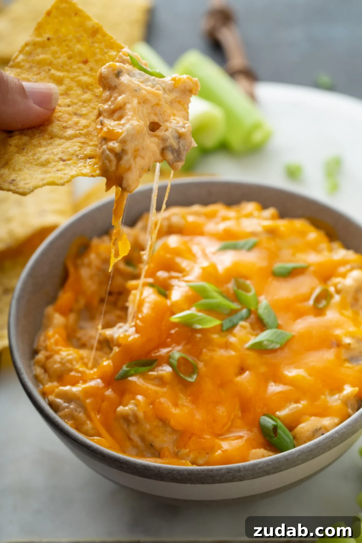 Slow Cooker Buffalo Chicken Dip Creamy Slow Cooker Buffalo Chicken Dip with a chip dipped in, showing melted cheese. Served with tortilla chips and celery sticks in the background.
