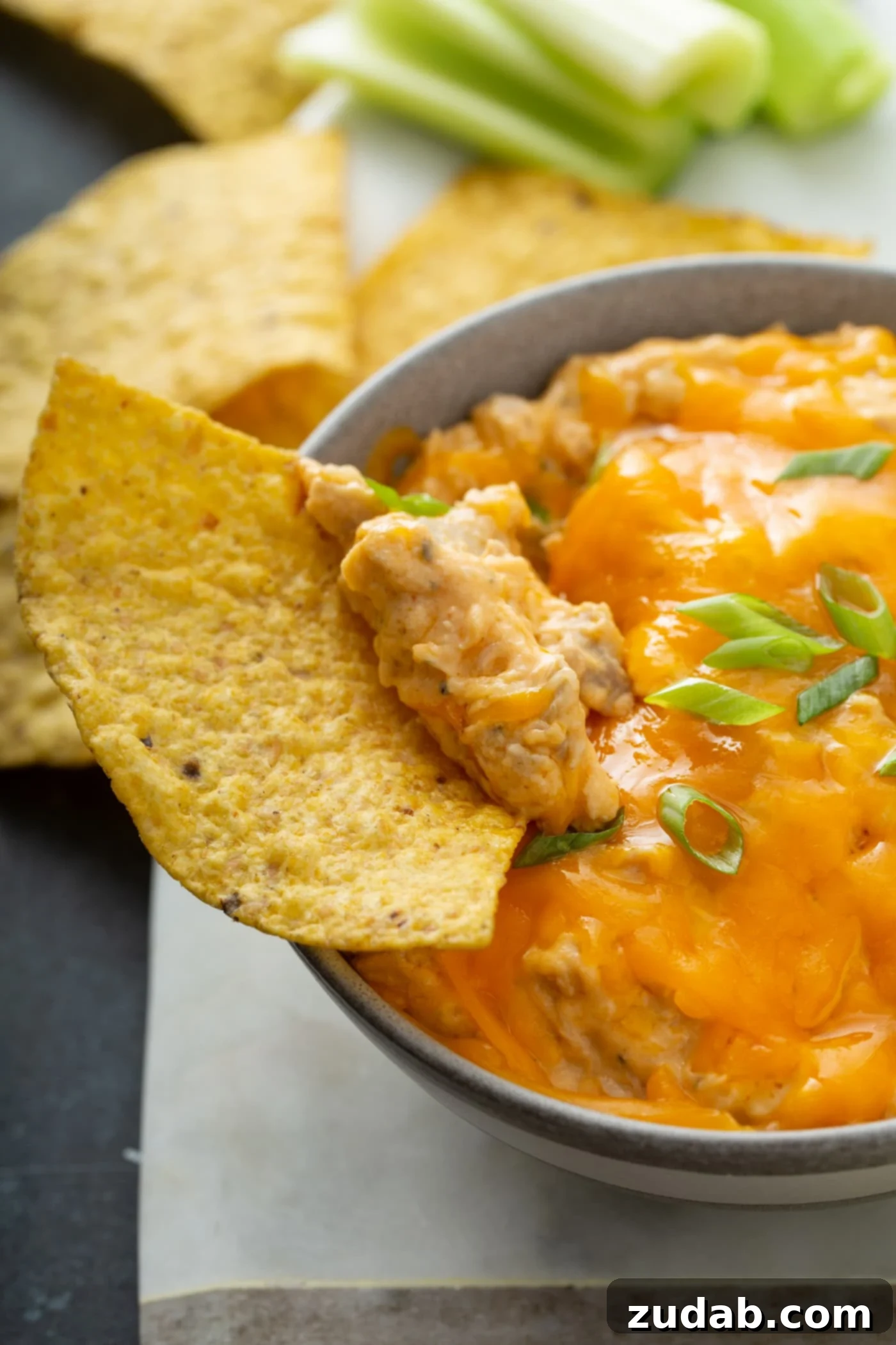 Slow Cooker Buffalo Chicken Dip A tortilla chip being dipped into a warm, gooey Slow Cooker Buffalo Chicken Dip, showing melted cheese and shredded chicken.