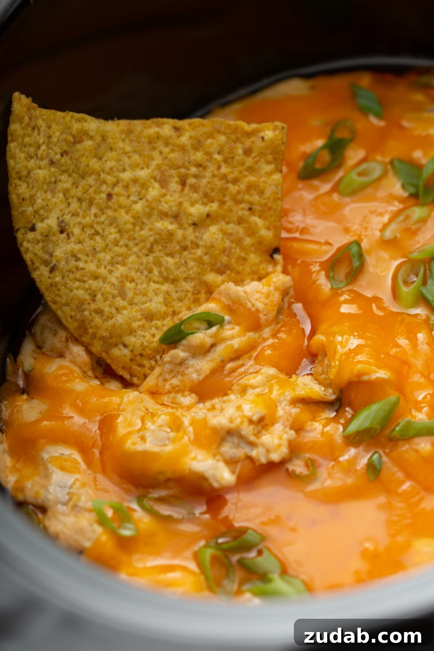 Slow Cooker Buffalo Chicken Dip Close-up of Slow Cooker Buffalo Chicken Dip with shredded chicken, creamy buffalo sauce, and chopped green onions on a tortilla chip.