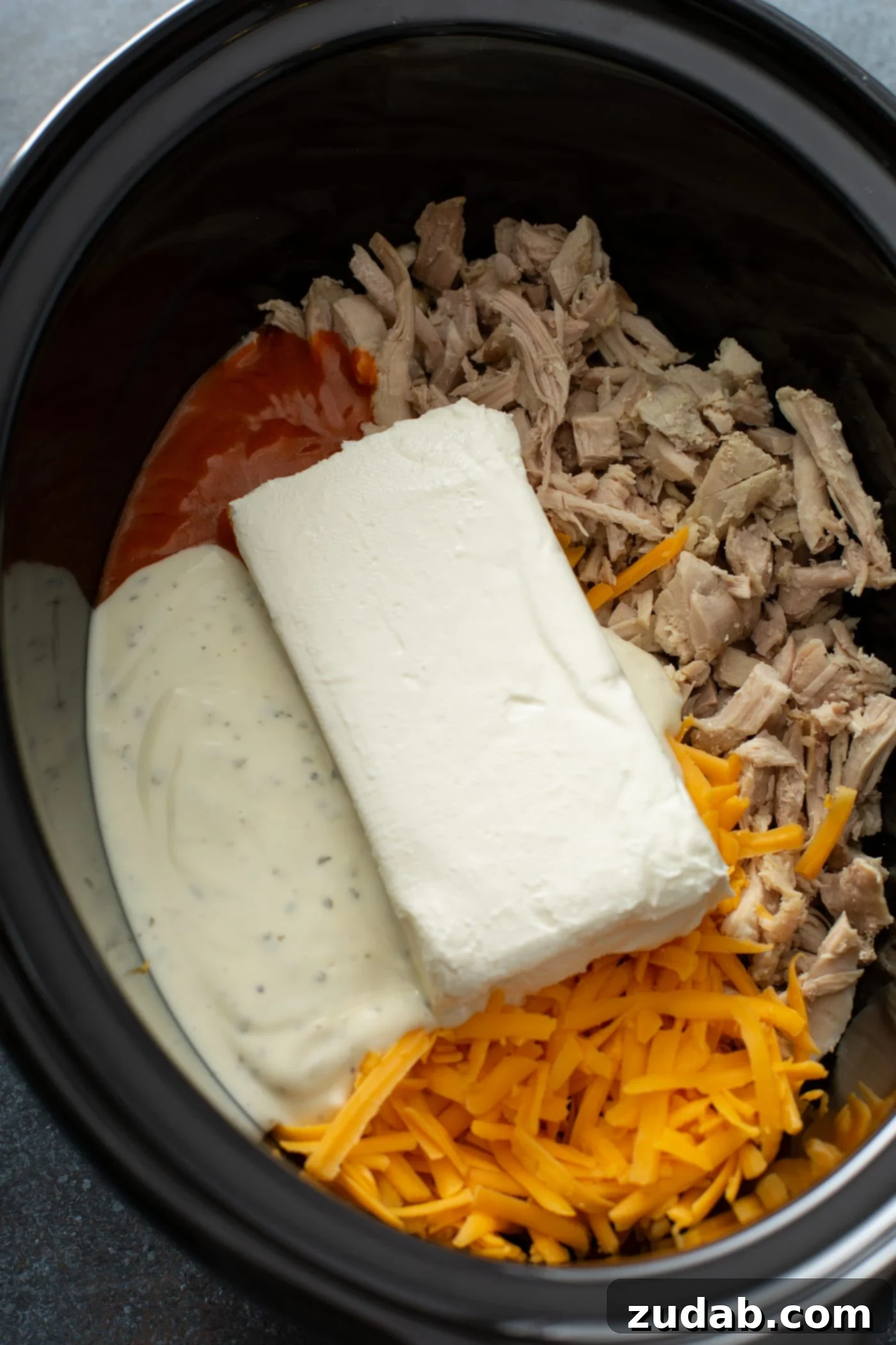 Slow Cooker Buffalo Chicken Dip Slow cooker pot filled with uncooked ingredients for Buffalo Chicken Dip: shredded chicken, cheeses, sauces, and butter.