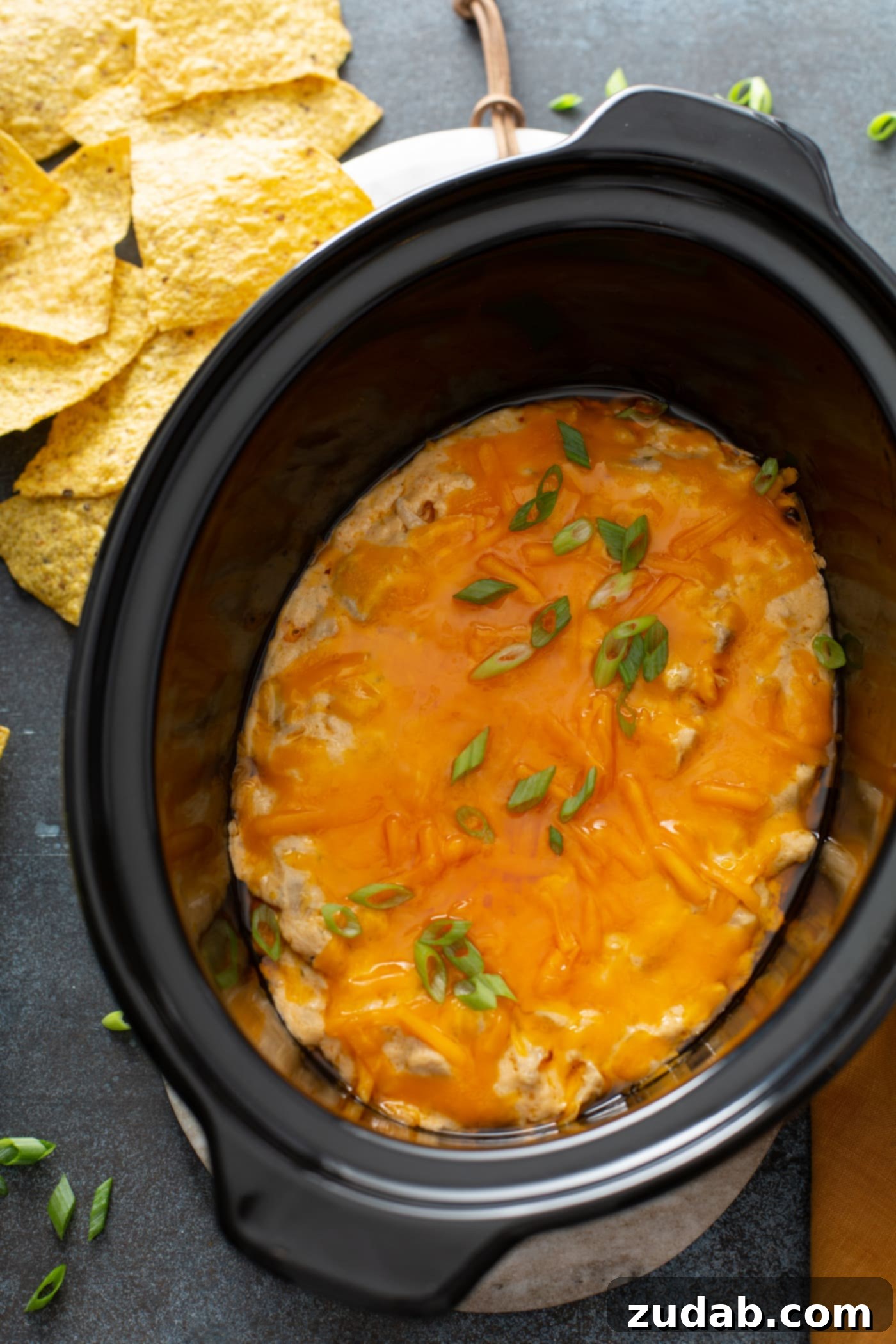 Slow Cooker Buffalo Chicken Dip Cooked and creamy Slow Cooker Buffalo Chicken Dip with melted cheese and green onions, ready to serve with tortilla chips in the background.