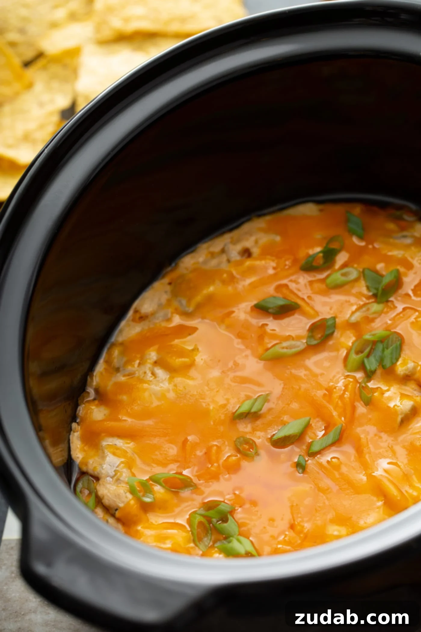 Slow Cooker Buffalo Chicken Dip Slow cooker filled with warm Buffalo Chicken Dip, ready to serve with tortilla chips next to it.
