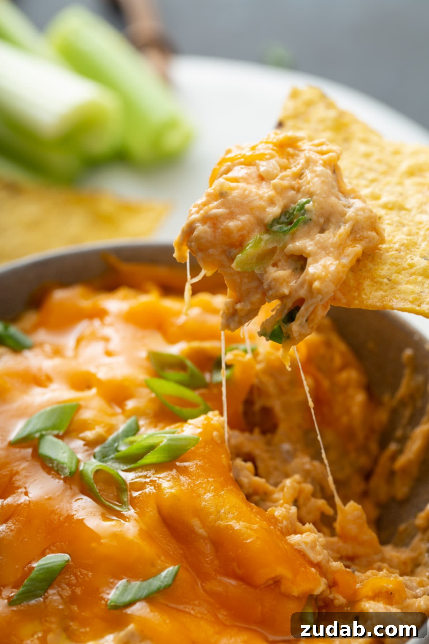 Slow Cooker Buffalo Chicken Dip Close-up of creamy Slow Cooker Buffalo Chicken Dip with shredded chicken, melted cheese, and green onions, a chip is scooping some dip.