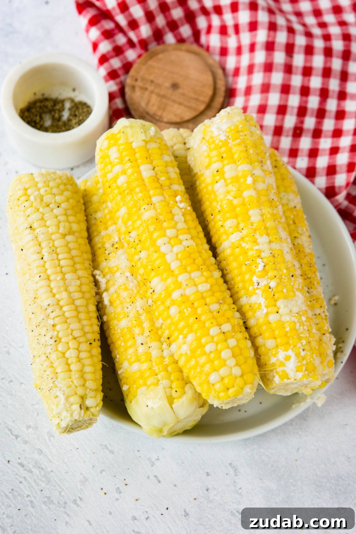 Easy Instant Pot Corn on the Cob 3 A serving plate with 5 ears of corn. The plate of corn is sitting on a red and white checked tea towel and there is a small container of