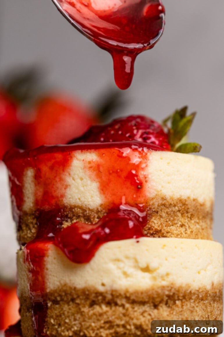 Luscious Strawberry Cheesecake Minis 7 A stack of mini cakes and a spoon dripping berry topping over top of the stack.