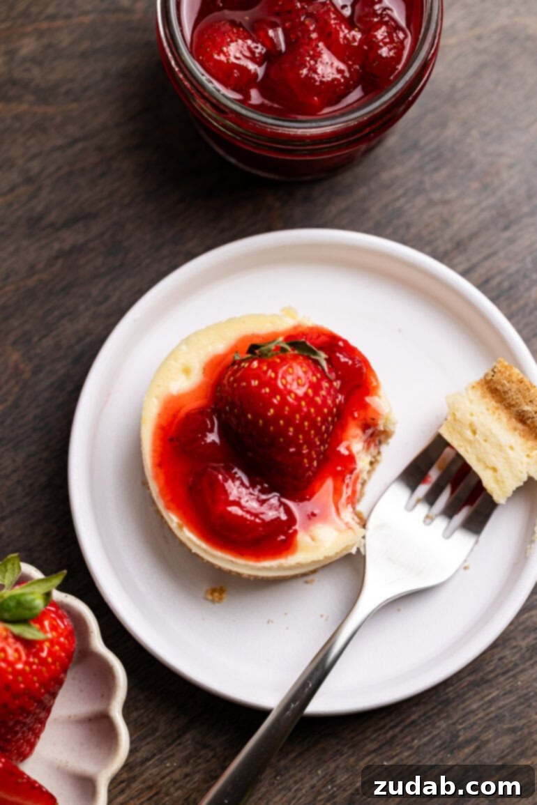 Luscious Strawberry Cheesecake Minis 8 A fork is taking a single bite out of a personal sized cheesecake with berry topping