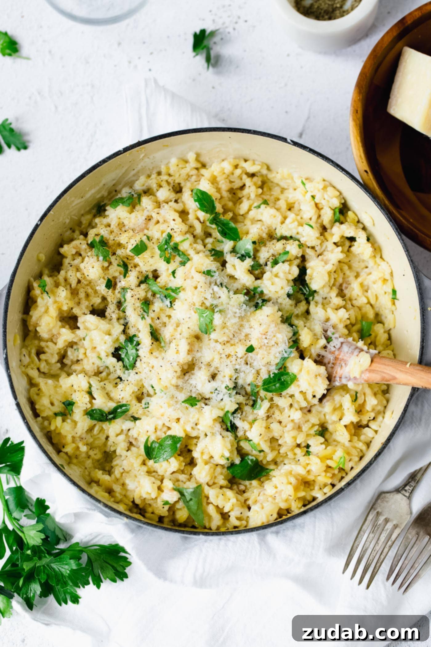 A serving bowl of creamy orzo. There is a wooden spoon in the pasta and the pasta is mixed in a creamy white sauce with fresh thyme leaves. There are fresh thyme leaves and a couple of forks laying next to the bowl.