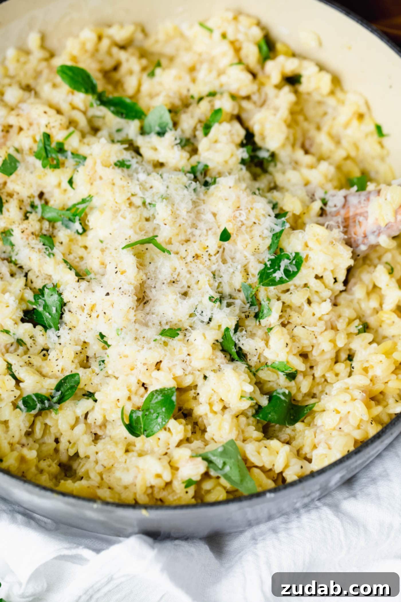 A close-up view of creamy garlic parmesan orzo. It is creamy and has fresh thyme leaves mixed into it.
