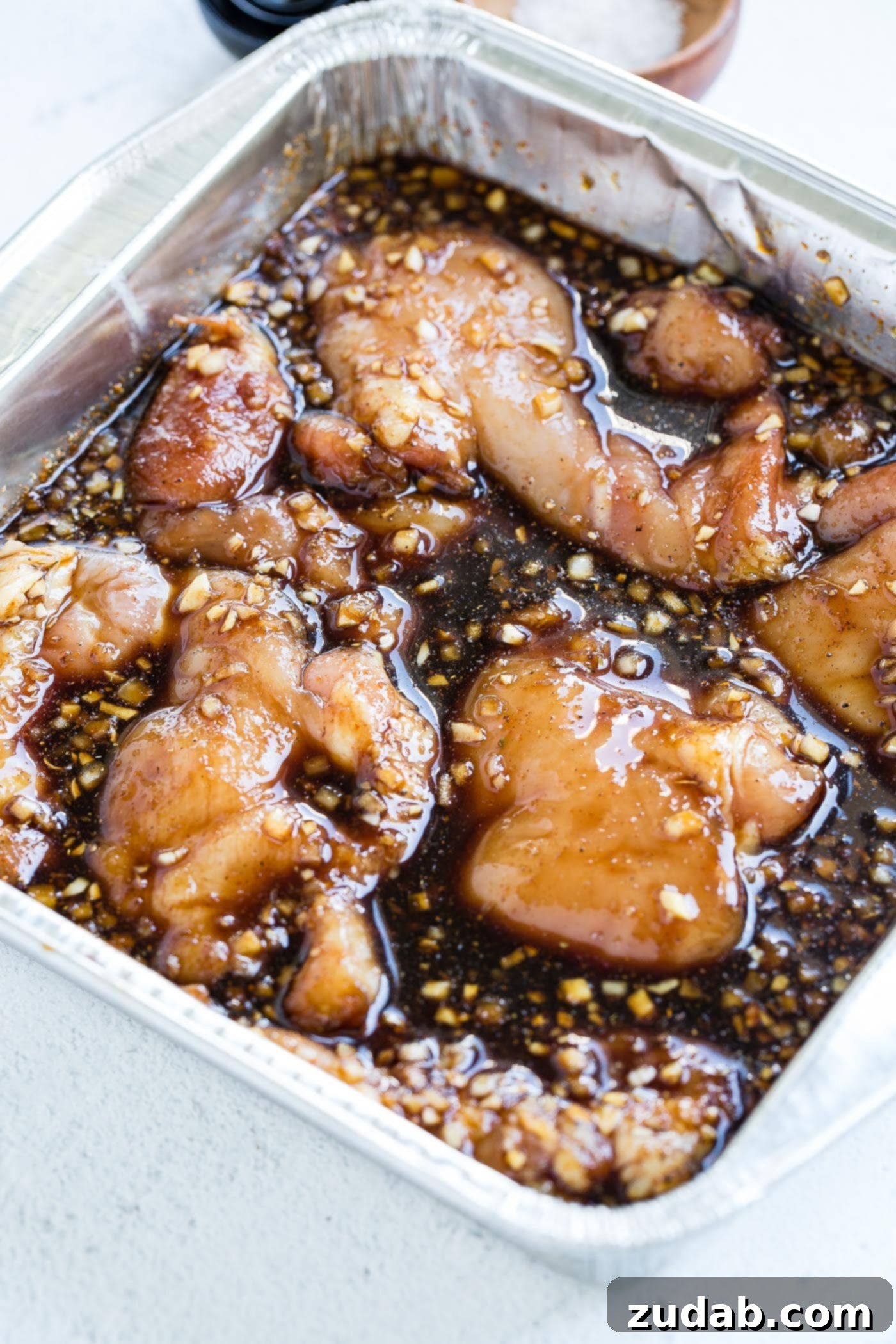 Marinated Smoked Chicken Thighs on the Traeger A large dish with chicken thighs marinating in a dark brown sauce.
