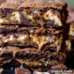 Decadent Snickers Caramel Brownies 2 A stack of cut brownies filled with melted caramel and snickers candy bars.