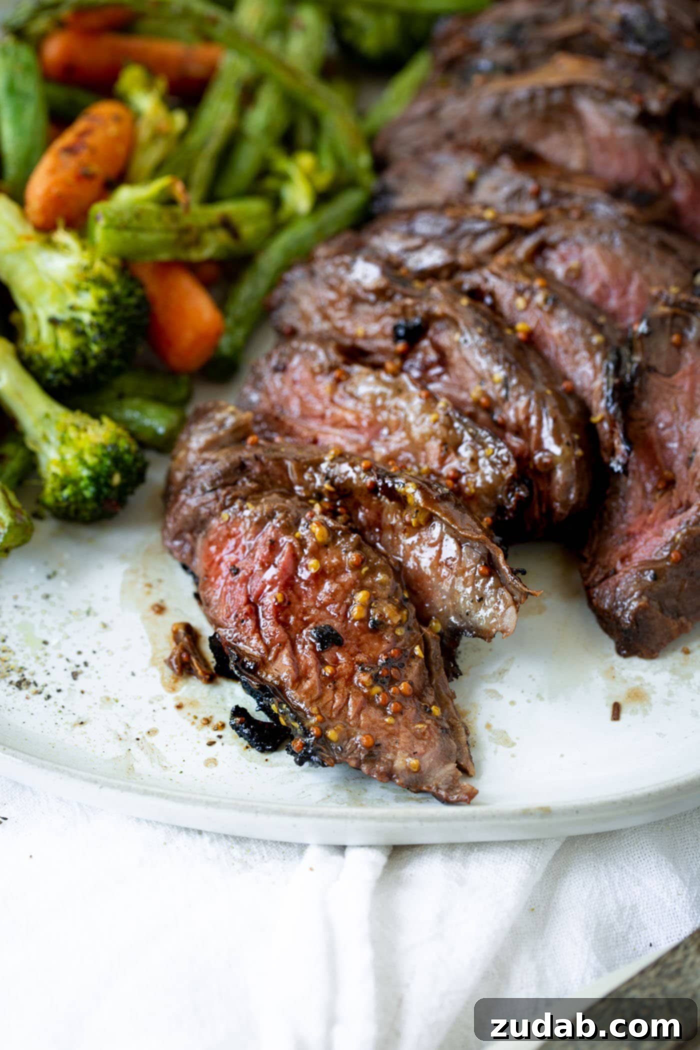 A close up photo of sliced medium rare hanger steak on a white plate next to some roasted vegetables.