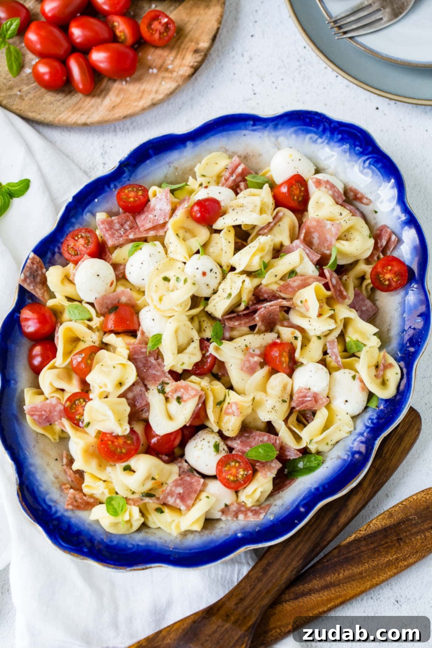 A serving dish of 5-minute Italian salami tortellini salad. There are chunks of salami, sliced tomatoes and mozzarella balls mixed in with the tender tortellini.