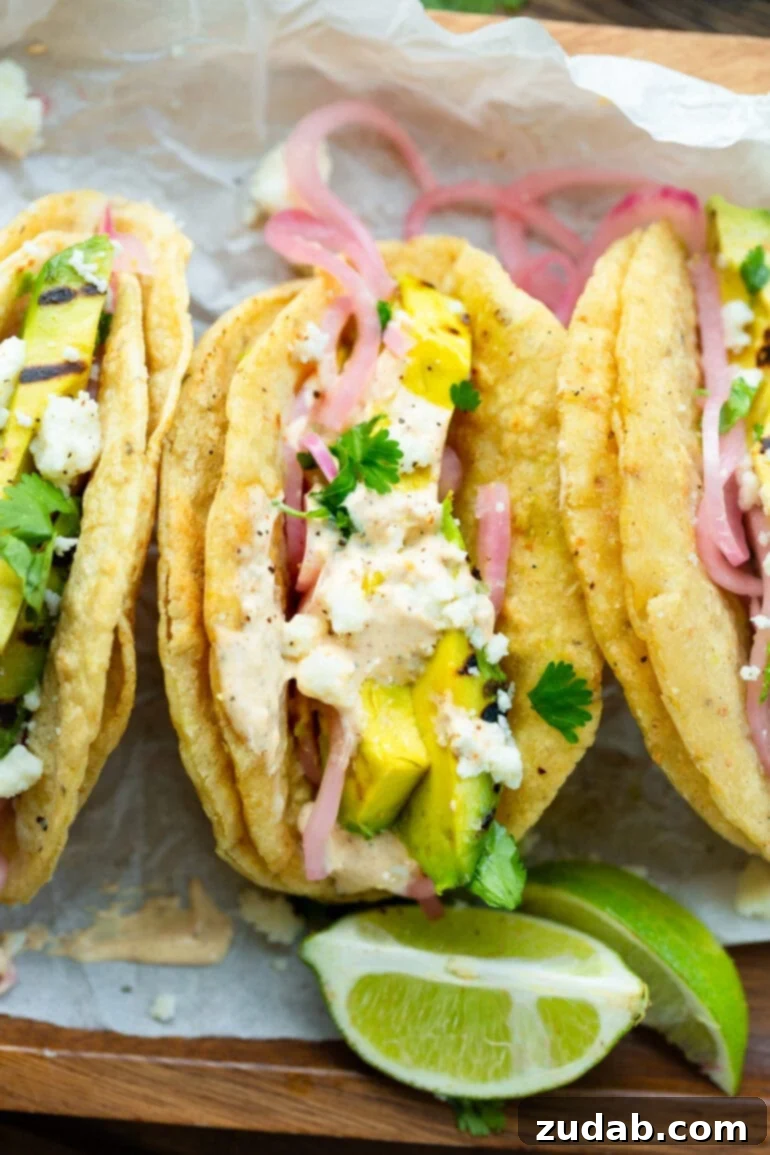 Smoky Grilled Avocado Tacos 4 a photo taken above three grilled avocado tacos in grilled corn tortillas topped with pickled onions, lime crema and crumbled queso fresco.