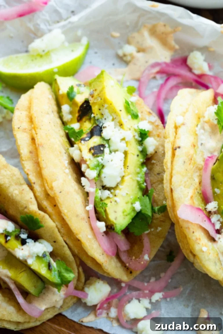Smoky Grilled Avocado Tacos 8 a close up photo of a grilled avocado taco topped with crumbled queso fresco and pickled onions in grilled corn tortillas
