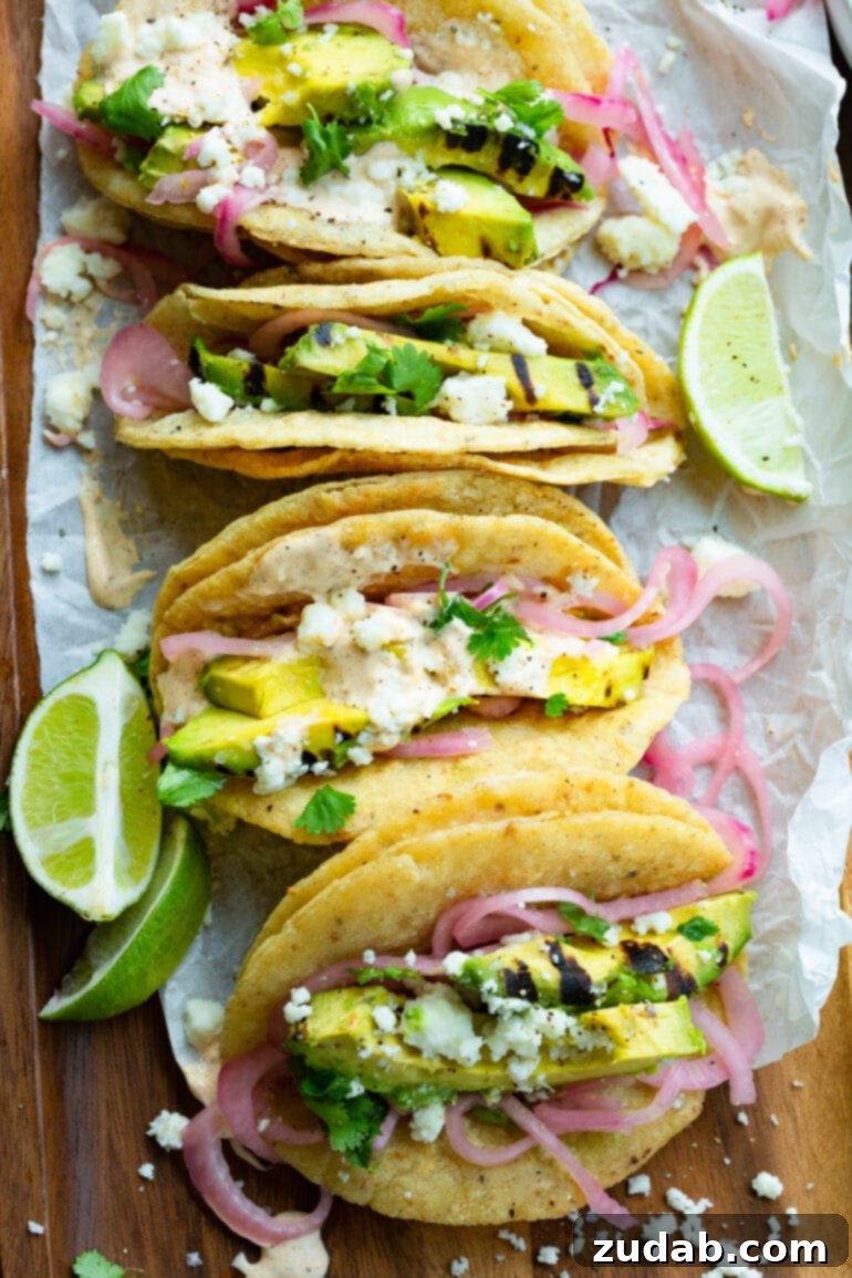 Smoky Grilled Avocado Tacos 9 a photo of several grilled avocados tacos lined up next to each other topped with pickled onions, lime crema, and queso fresco.