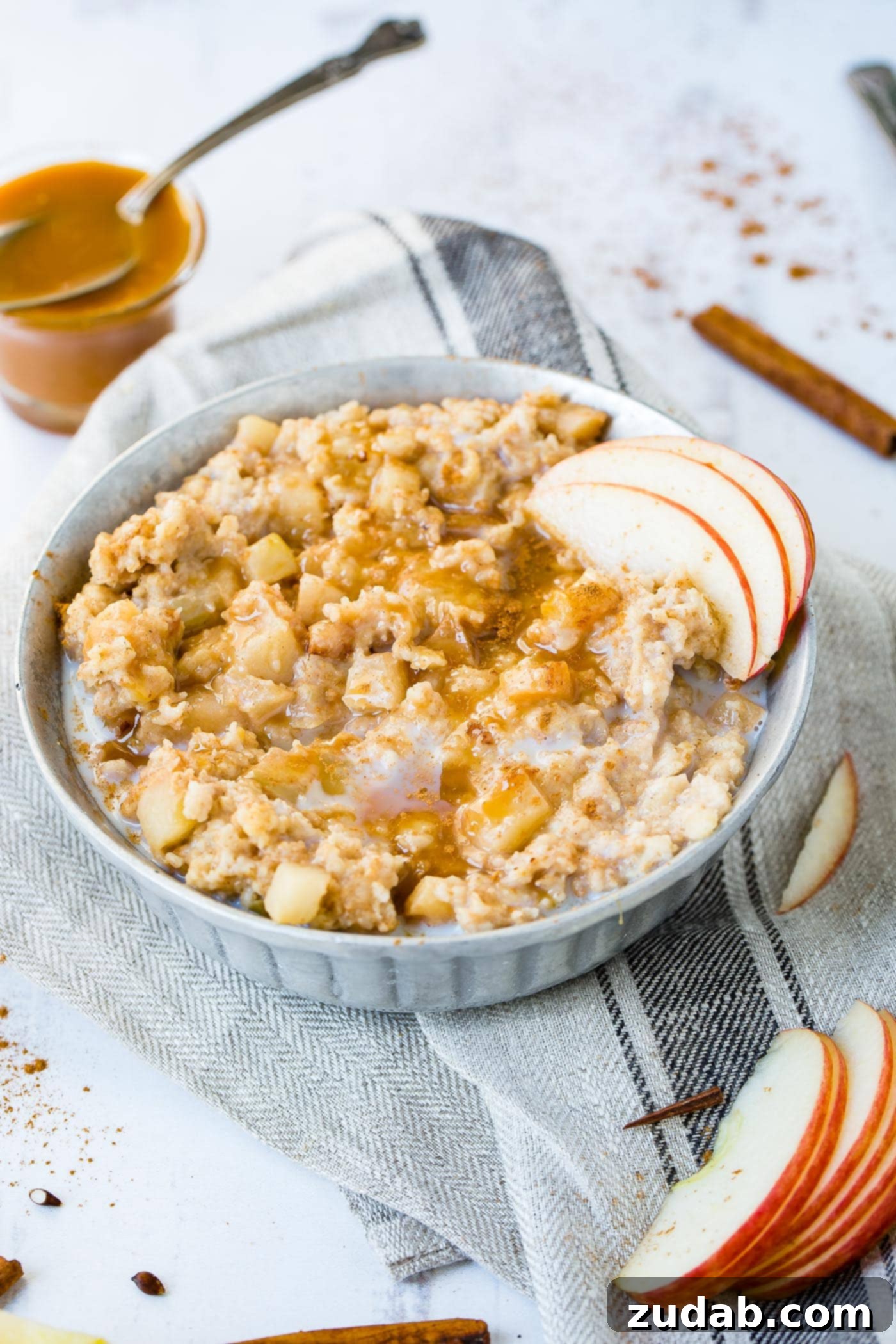 Apple Pie Slow Cooker Oatmeal A photo of a bowl of oatmeal full of apple chunks and topped with caramel and thin apple slices.