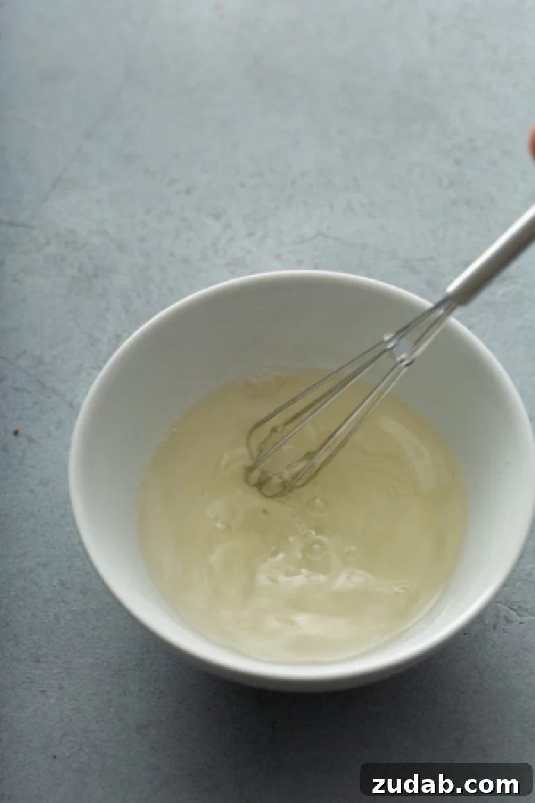 The Ultimate Guide to Foolproof Whipped Cream Stability 3 A white mixing bowl with a whisk and partially whipped cream