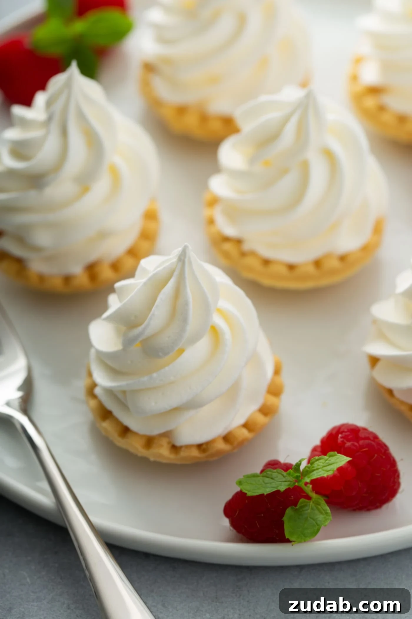 Dessert Topping Ideas A few little tarts with whipped cream piped on top. There are a few raspberries next to the tarts.
