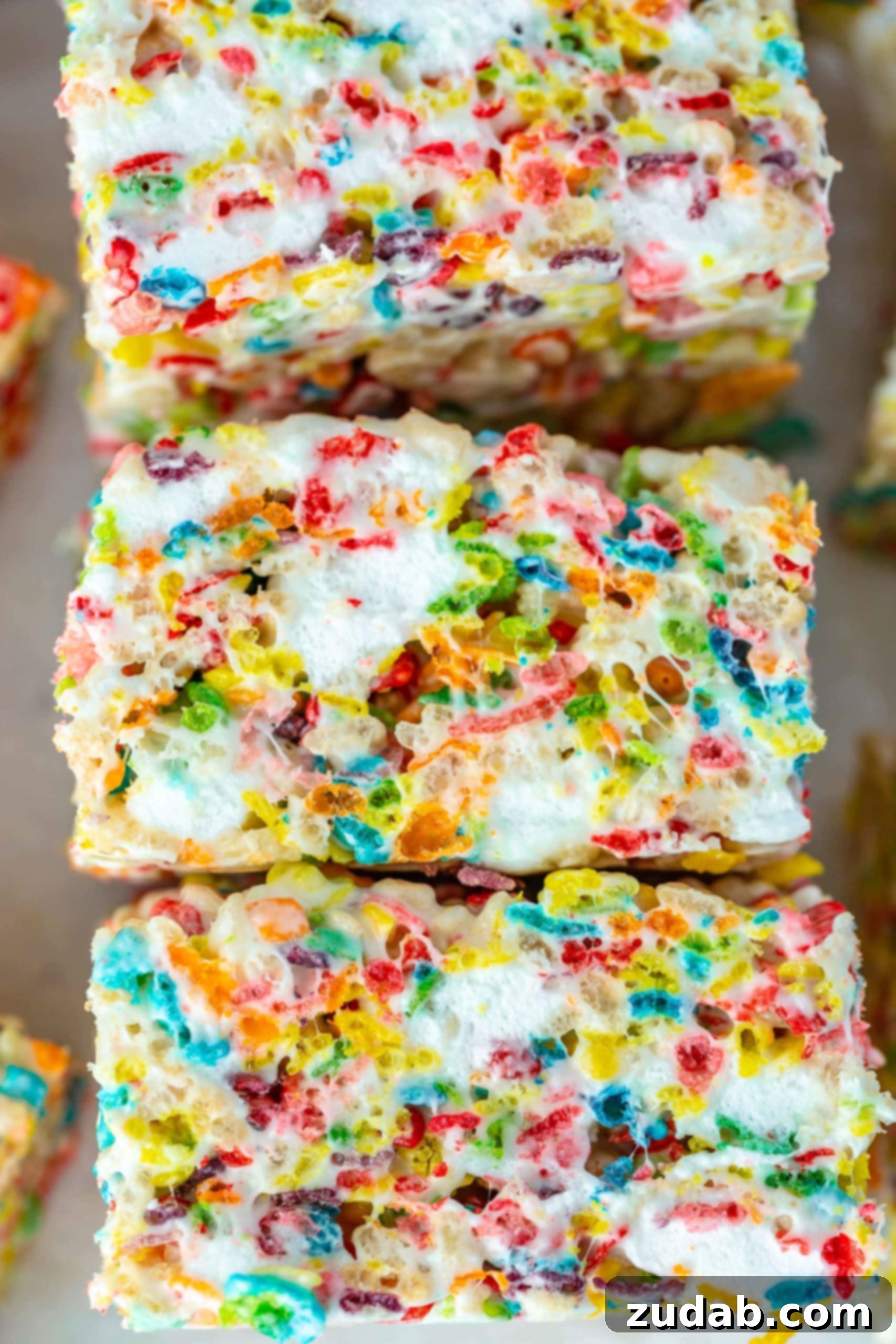 Fruity Pebbles Rice Krispy Treats Stack Three squares of vibrant Fruity Pebbles Rice Krispie treats stacked, showcasing the gooey marshmallow holding the colorful cereal together.