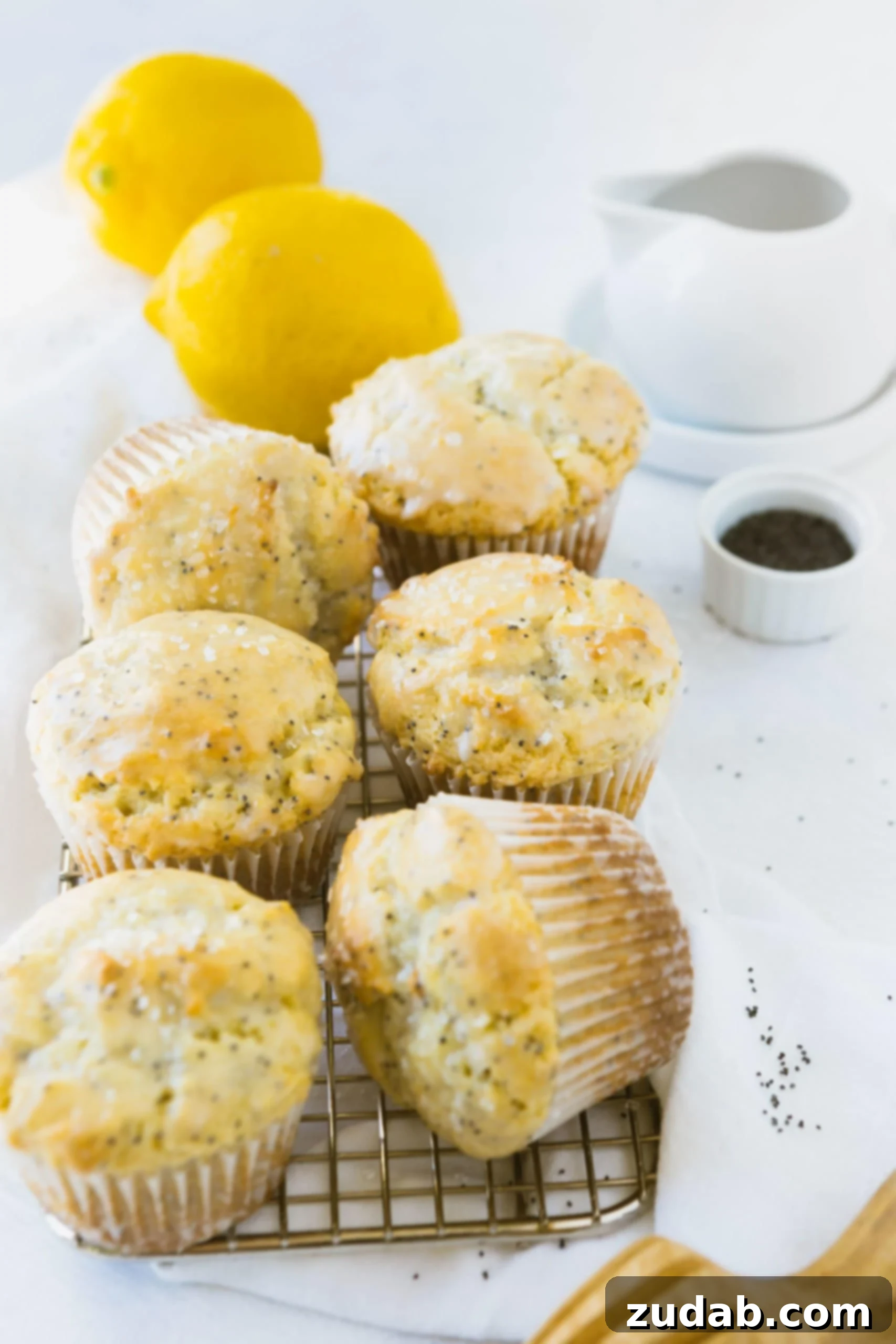 Zesty Lemon Poppy Seed Muffins 2 6 lemon poppy seed muffins with lemon glaze. There are two lemons in the background.