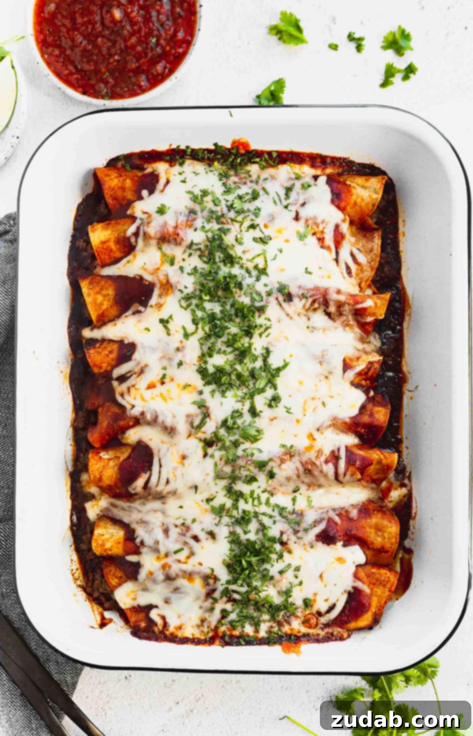Family Favorite Cheesy Ground Beef Enchiladas a photo of a pan of ground beef enchiladas from overhead covered in melted cheese and chopped cilantro with a cup of salsa next to the pan.