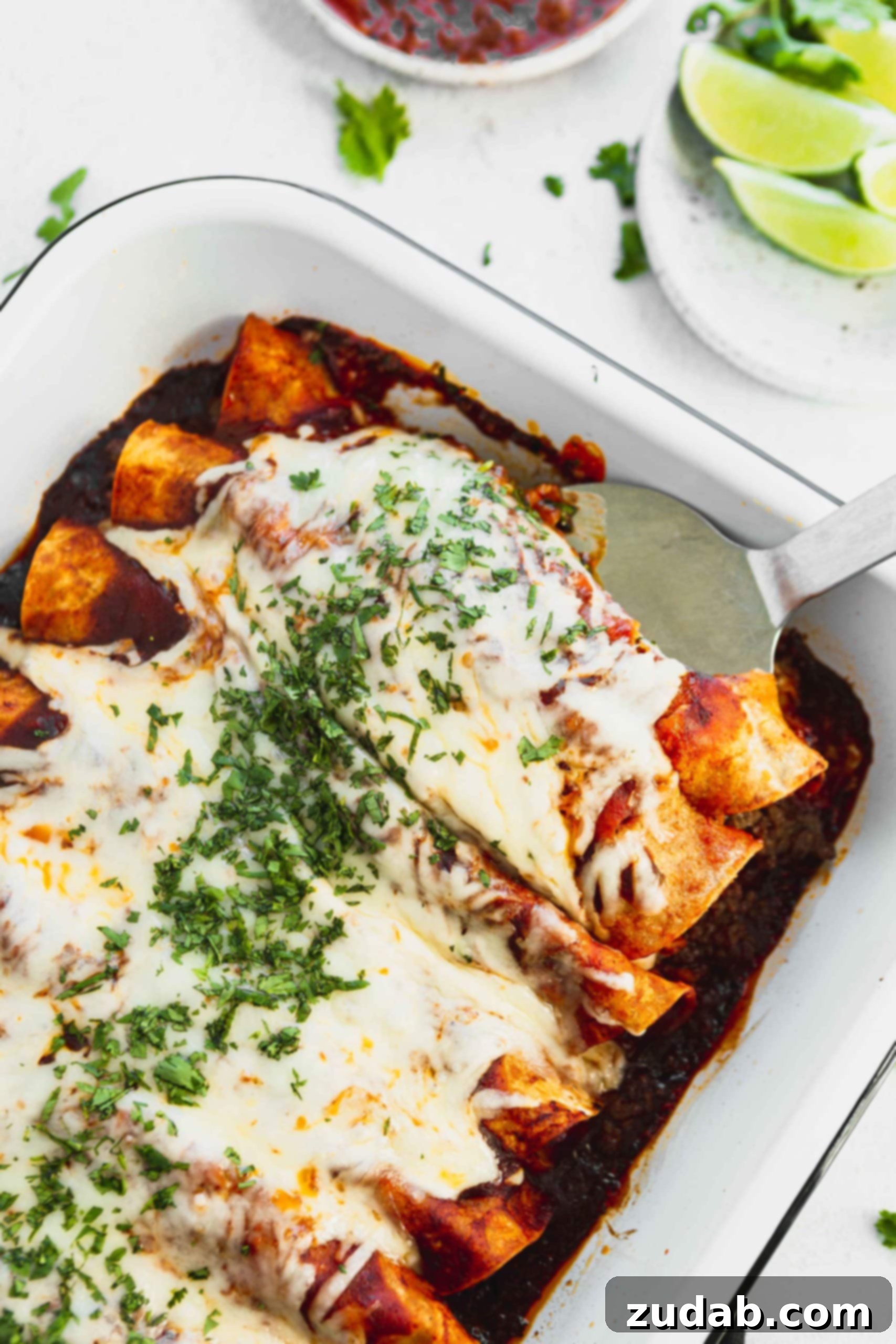 Family Favorite Cheesy Ground Beef Enchiladas A photo of a pan of ground beef enchiladas with the first two being removed with a metal spatula.
