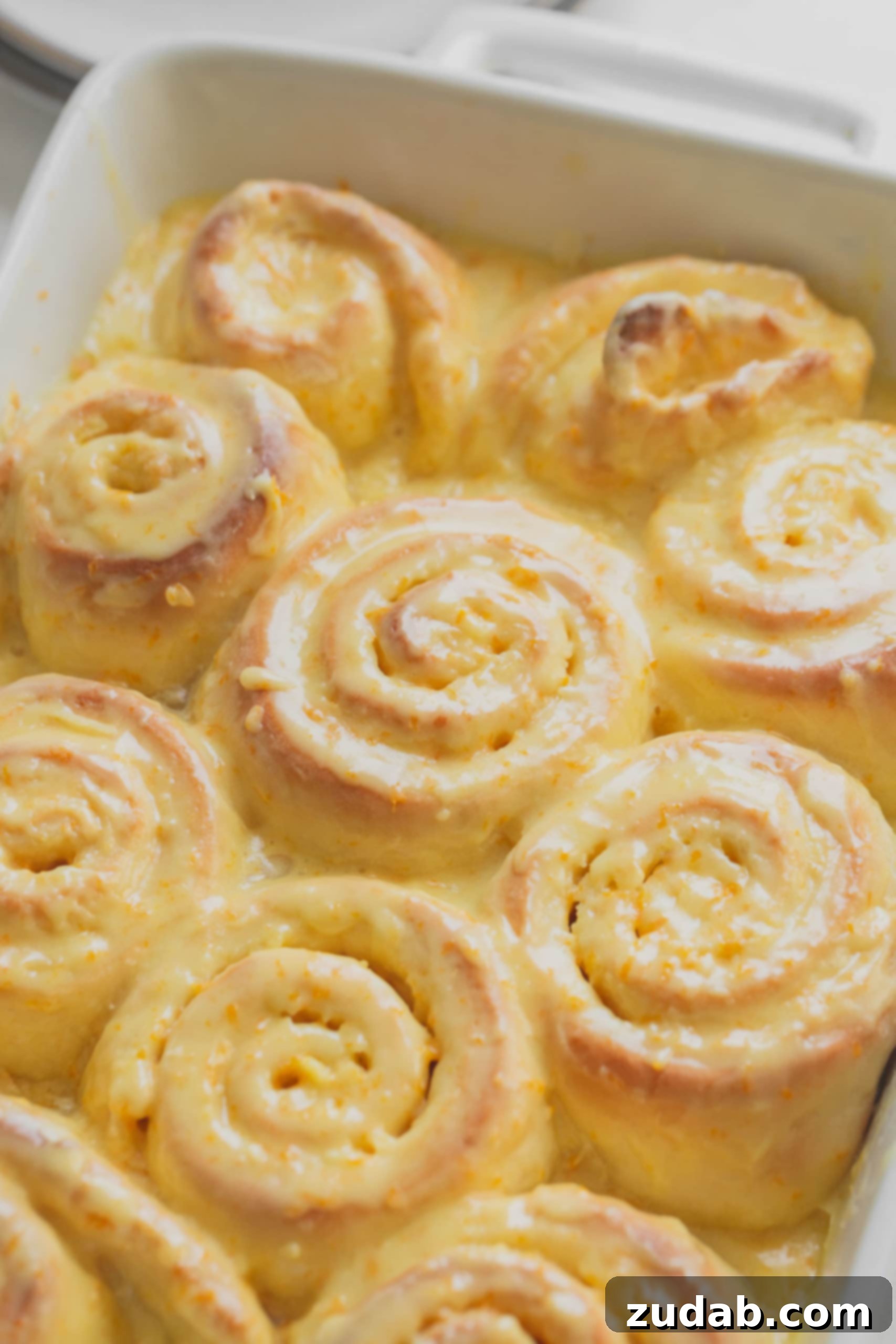 Orange Rolls A pan of baked, glazed orange rolls. They are golden brown with an orange glaze filled with bits of orange zest.