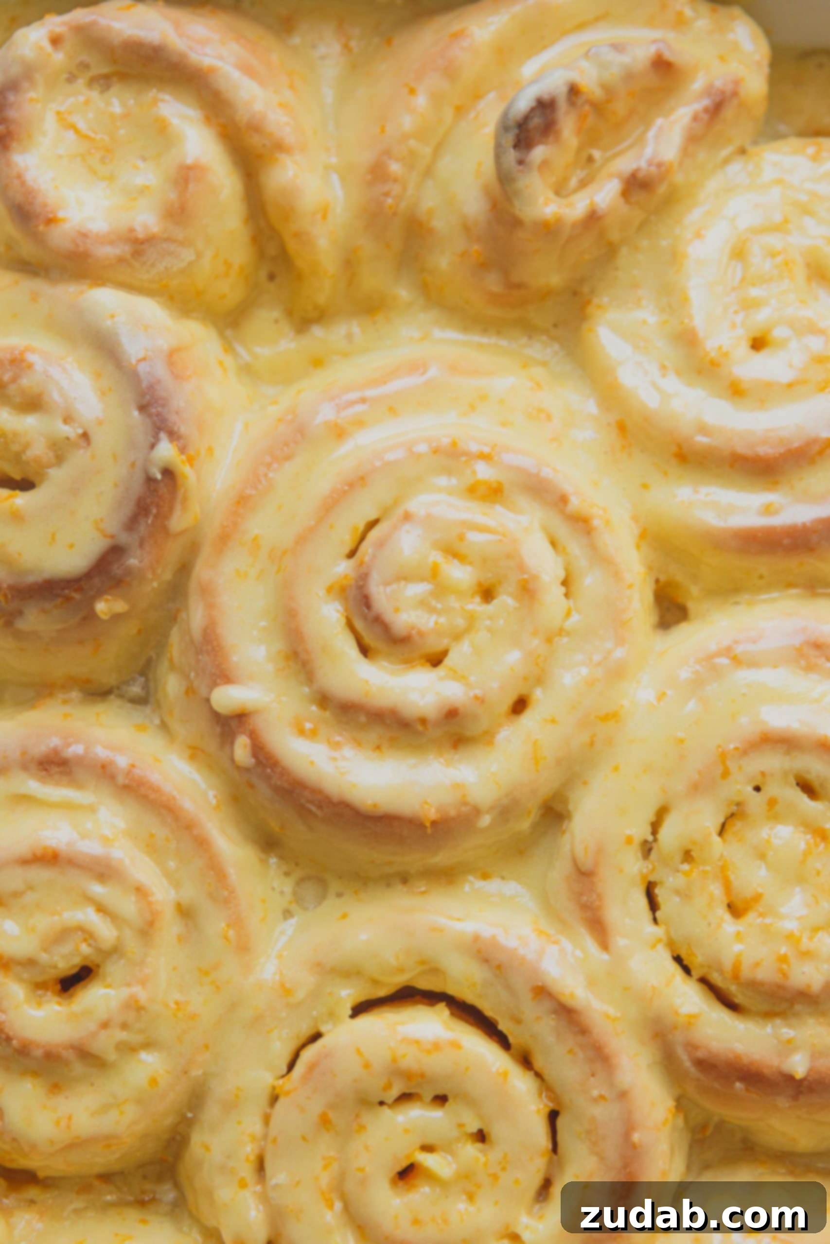 Orange Rolls A close up, top view of a pan of orange rolls. They are topped with orange frosting.