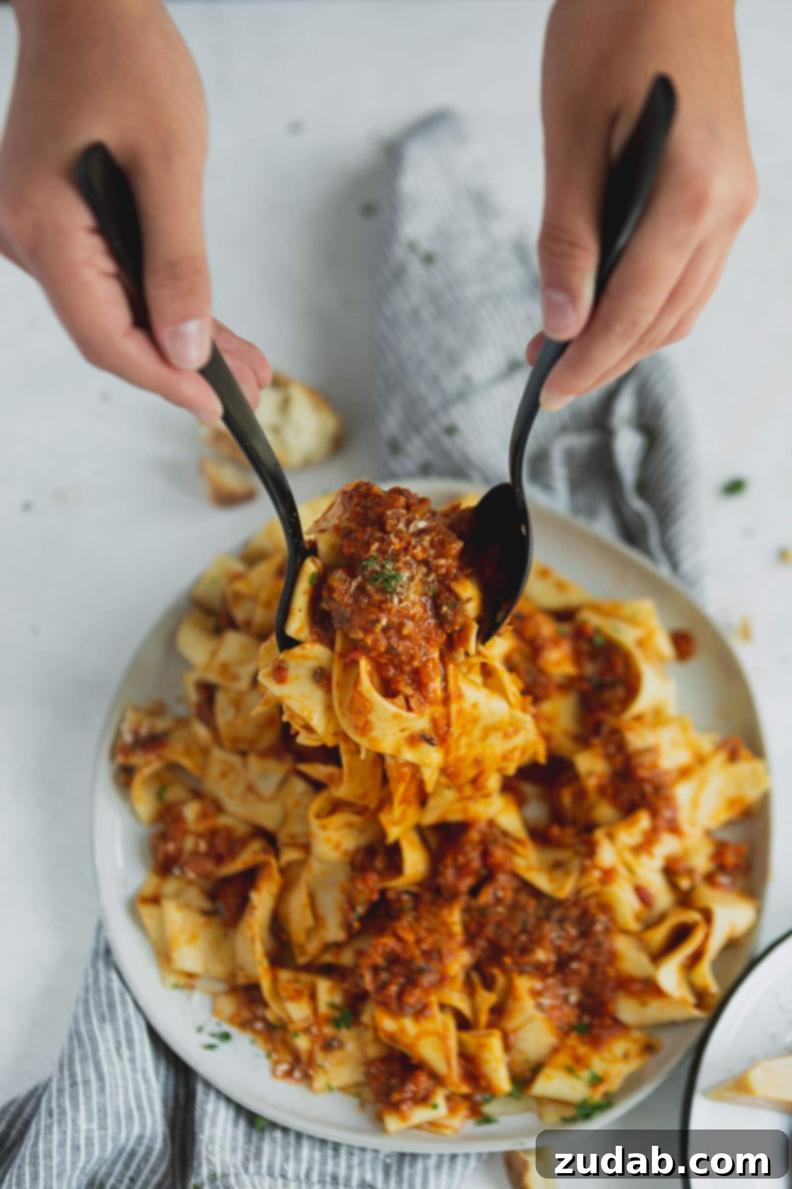 Serving Plant-Based Bolognese Pasta A serving plate piled high with pasta and vegan bolognese sauce, presented with two serving spoons.