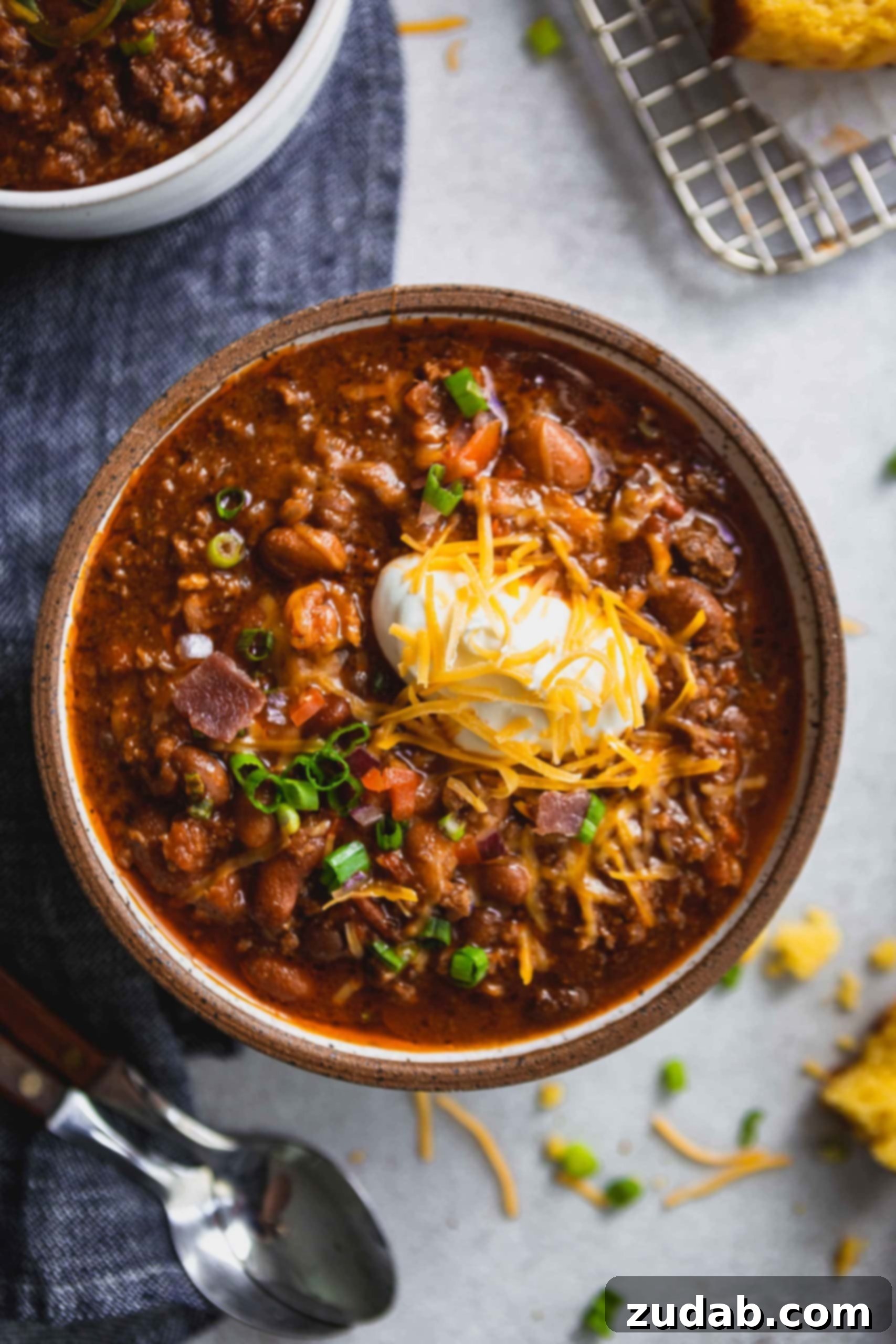 The Ultimate Chili Recipe 3 A bowl of the best chili. There is ground beef, three kinds of beans, spices, sour cream and grated cheese on top.