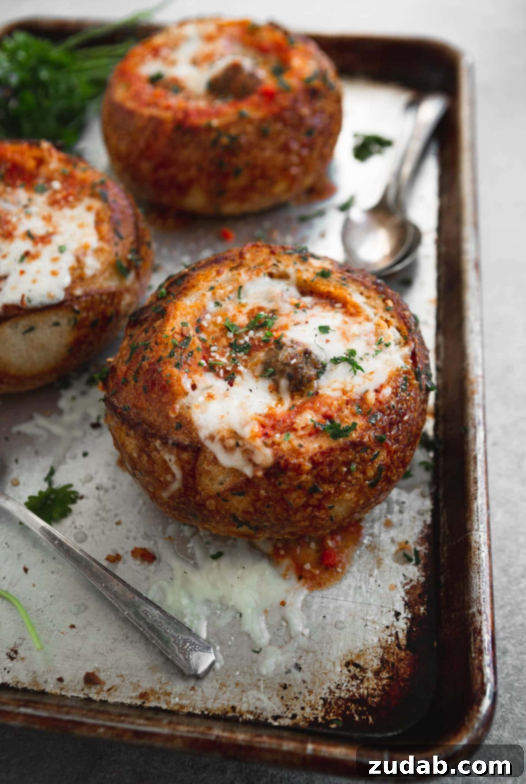 Parmesan Meatball Soup Three toasted bread bowls filled with meatball parmesan soup. there is melted cheese sprinkled with fresh parsley on top.