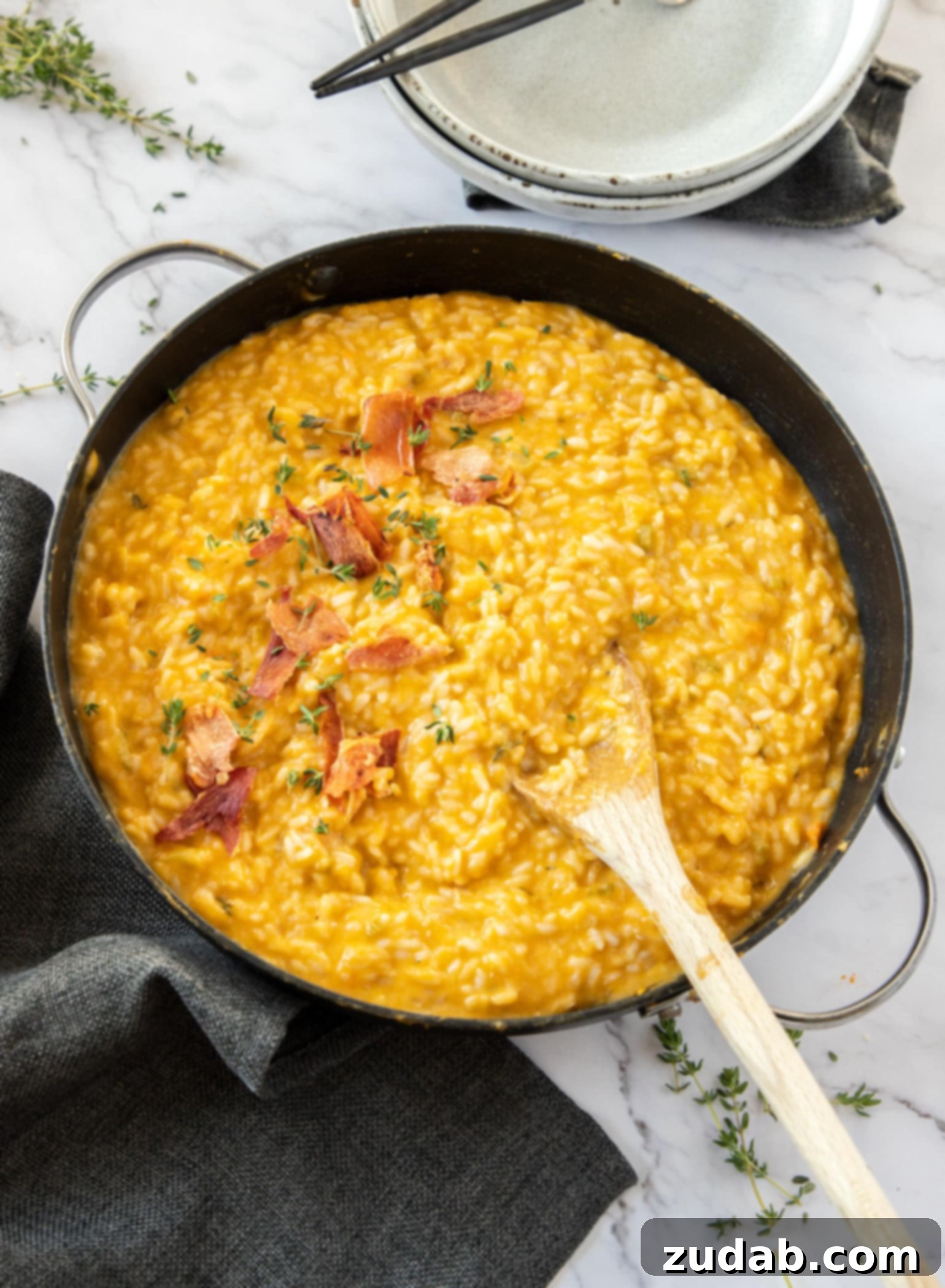 A large skillet filled with orange coloured risotto. Bowls and herbs are strewn around.